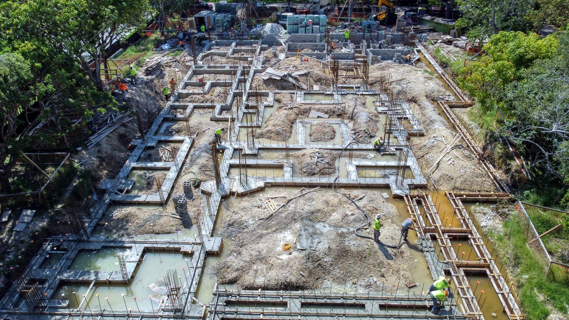 Construction site with foundation forms, muddy ground, and workers.