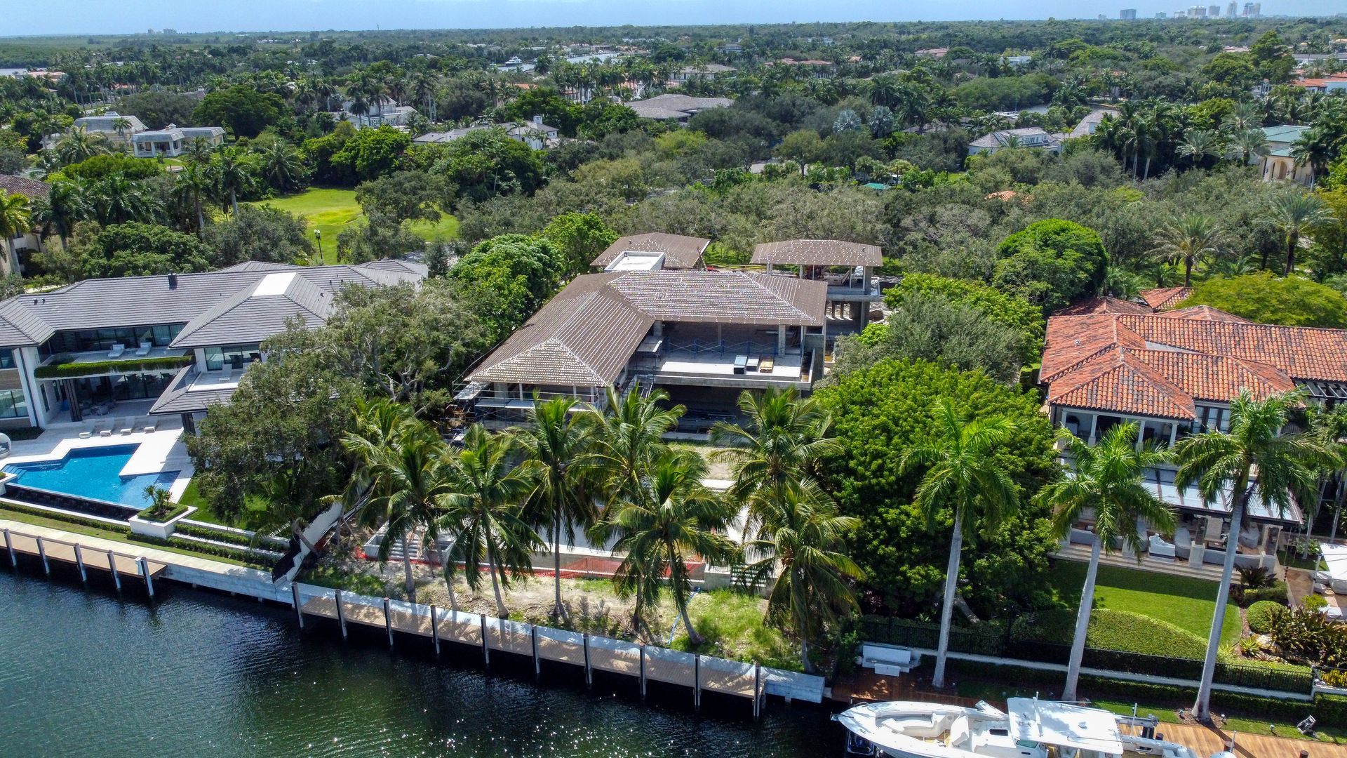 Aerial view of waterfront luxury homes with boats docked along a canal, lush green trees.