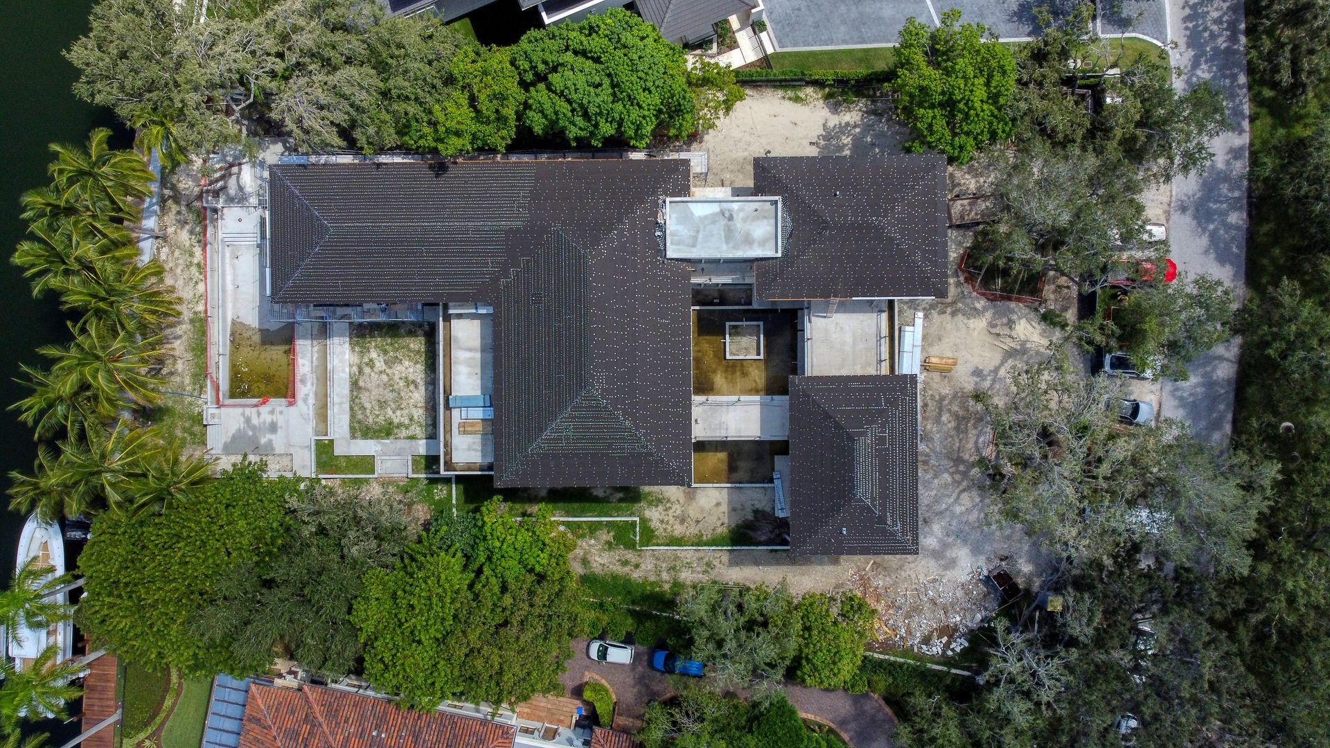 Aerial view of a home with a dark roof and surrounding trees and landscaping, near water.