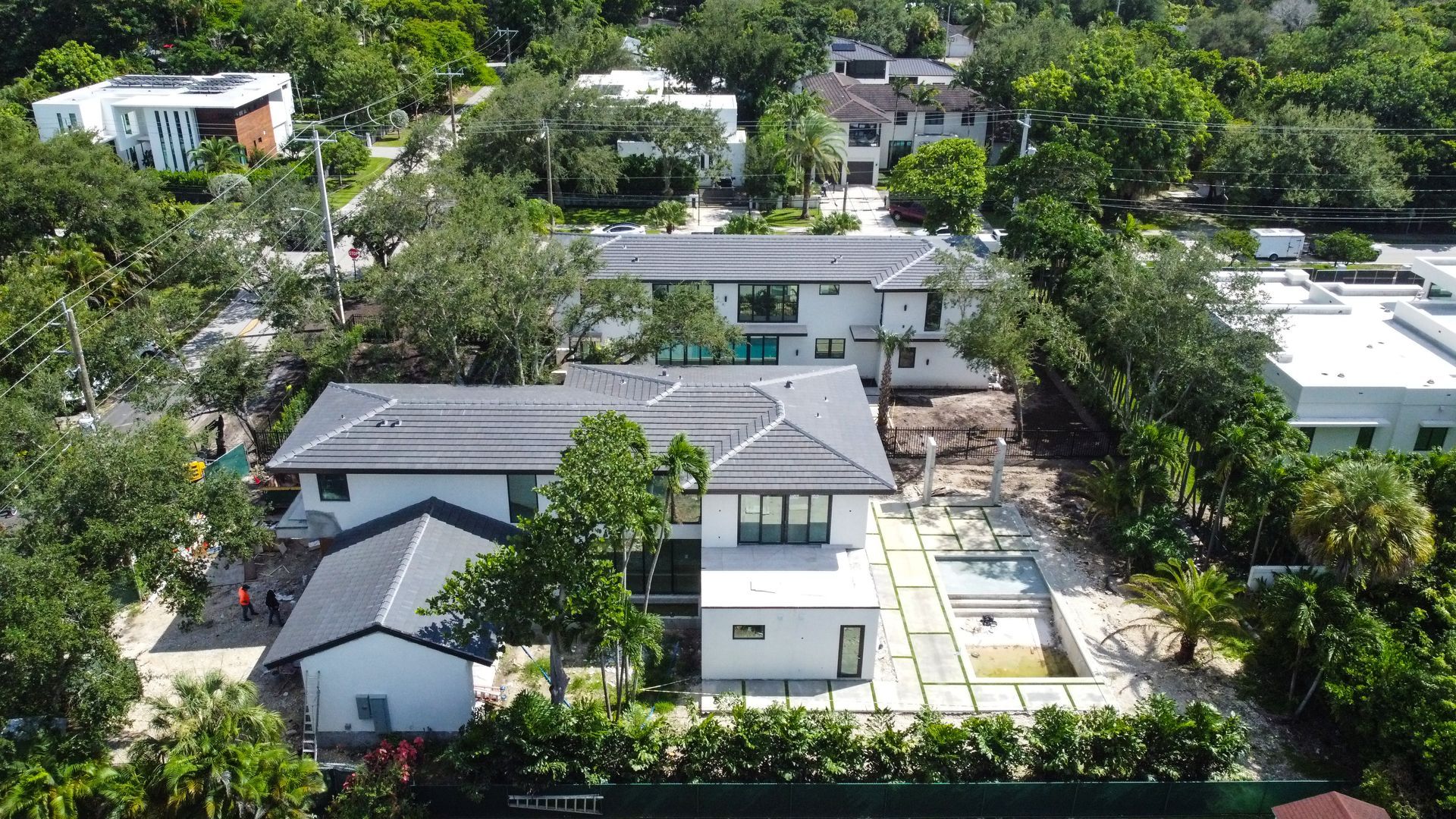 Aerial view of modern white houses with swimming pool, surrounded by lush green trees.