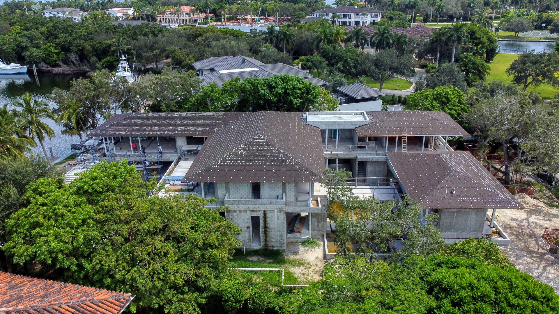 Overhead view of a large, weathered, multi-level house surrounded by lush greenery and a body of water.