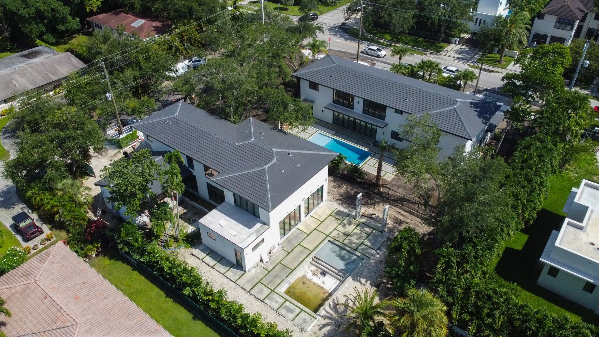 Aerial view of two modern homes with pools and trees in a residential neighborhood.