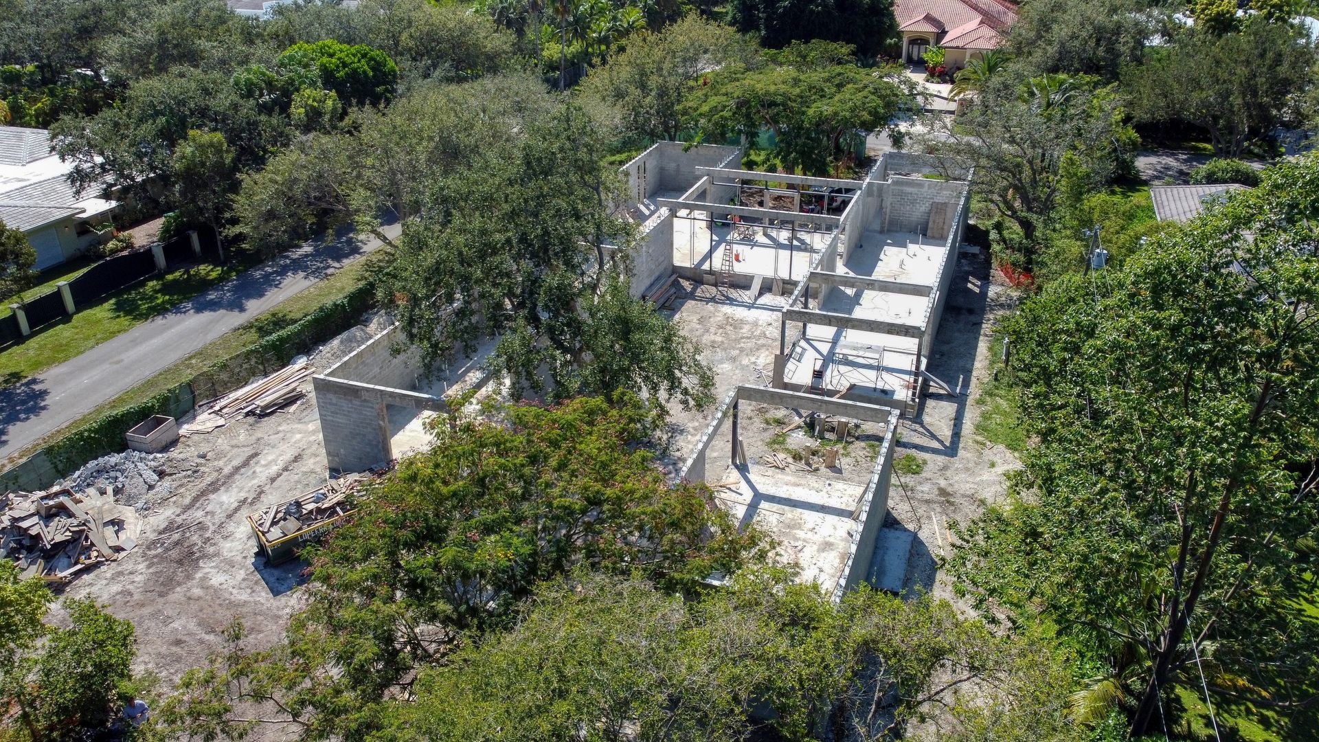Aerial view of a house under construction; concrete framework surrounded by trees and a dirt lot.