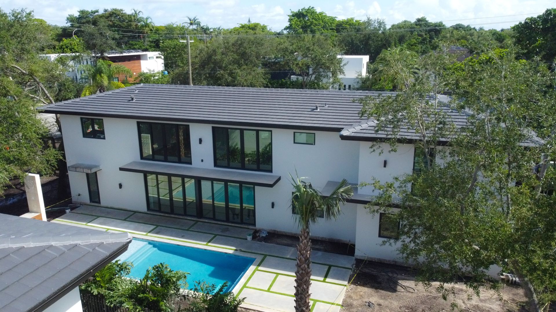 Two-story white house with dark roof and large windows, a pool, and surrounding trees.