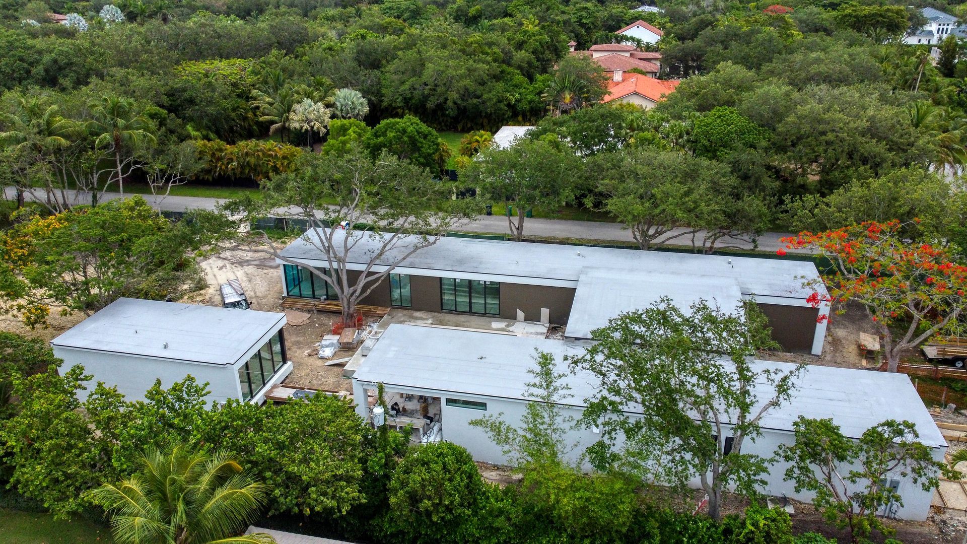 Aerial view of a contemporary home under construction, surrounded by lush green trees and foliage.