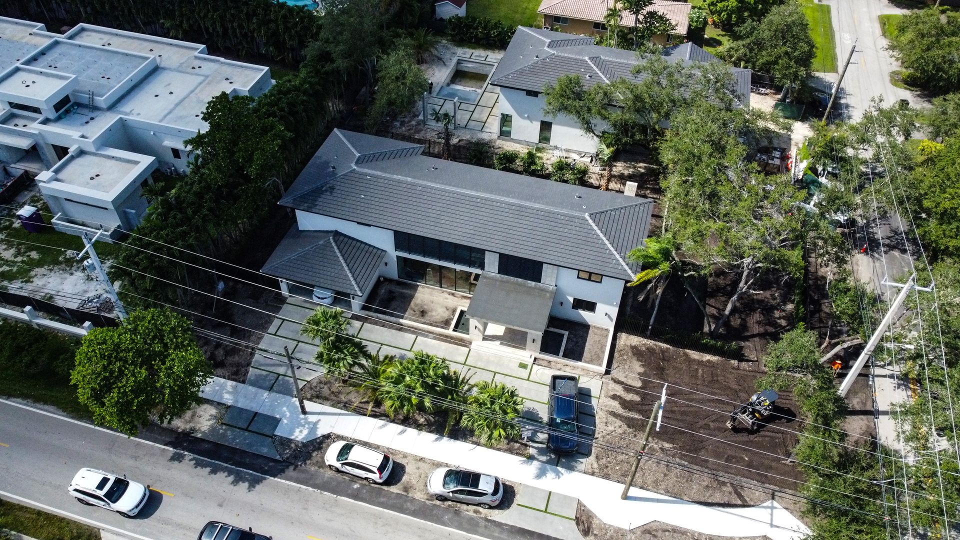 Aerial view of a modern white house with a dark roof and a driveway lined with parked cars.