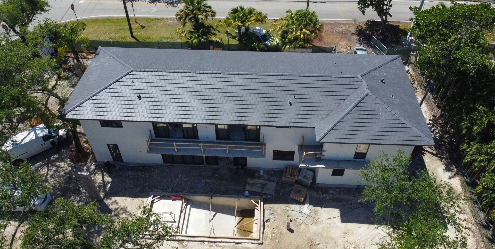 Aerial view of a gray roofed house under construction with a surrounding road and trees.