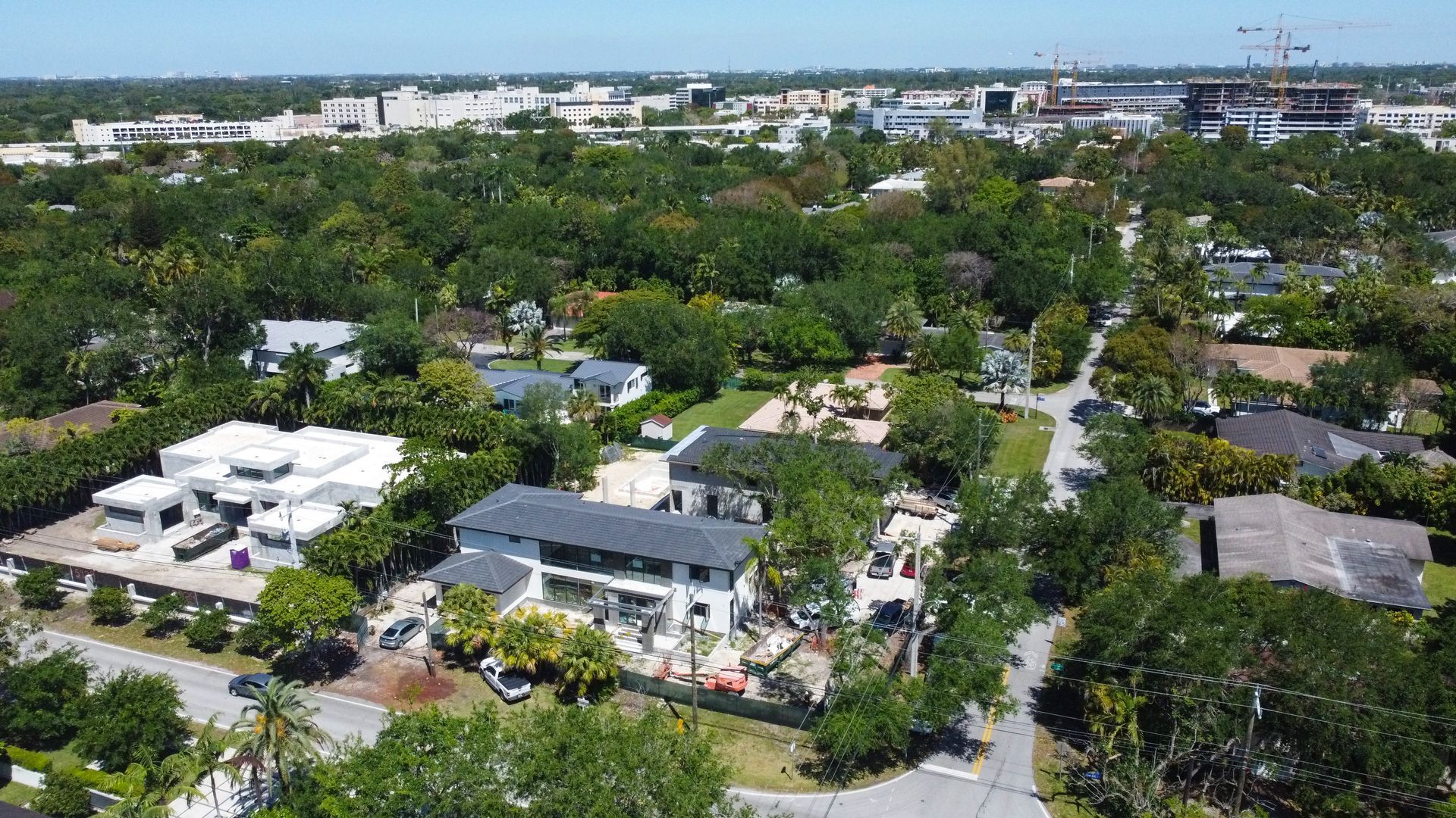 Aerial view of residential neighborhood with trees and houses, under a bright, sunny sky.