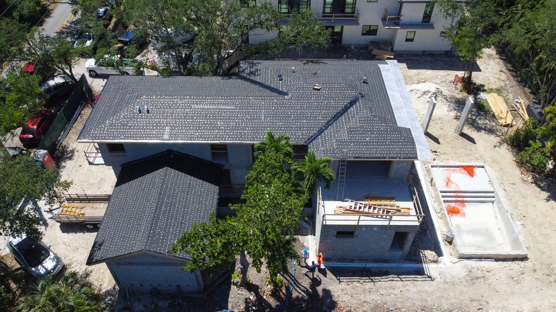 Aerial view of a house under construction with a dark gray roof and concrete walls, trees surround it.