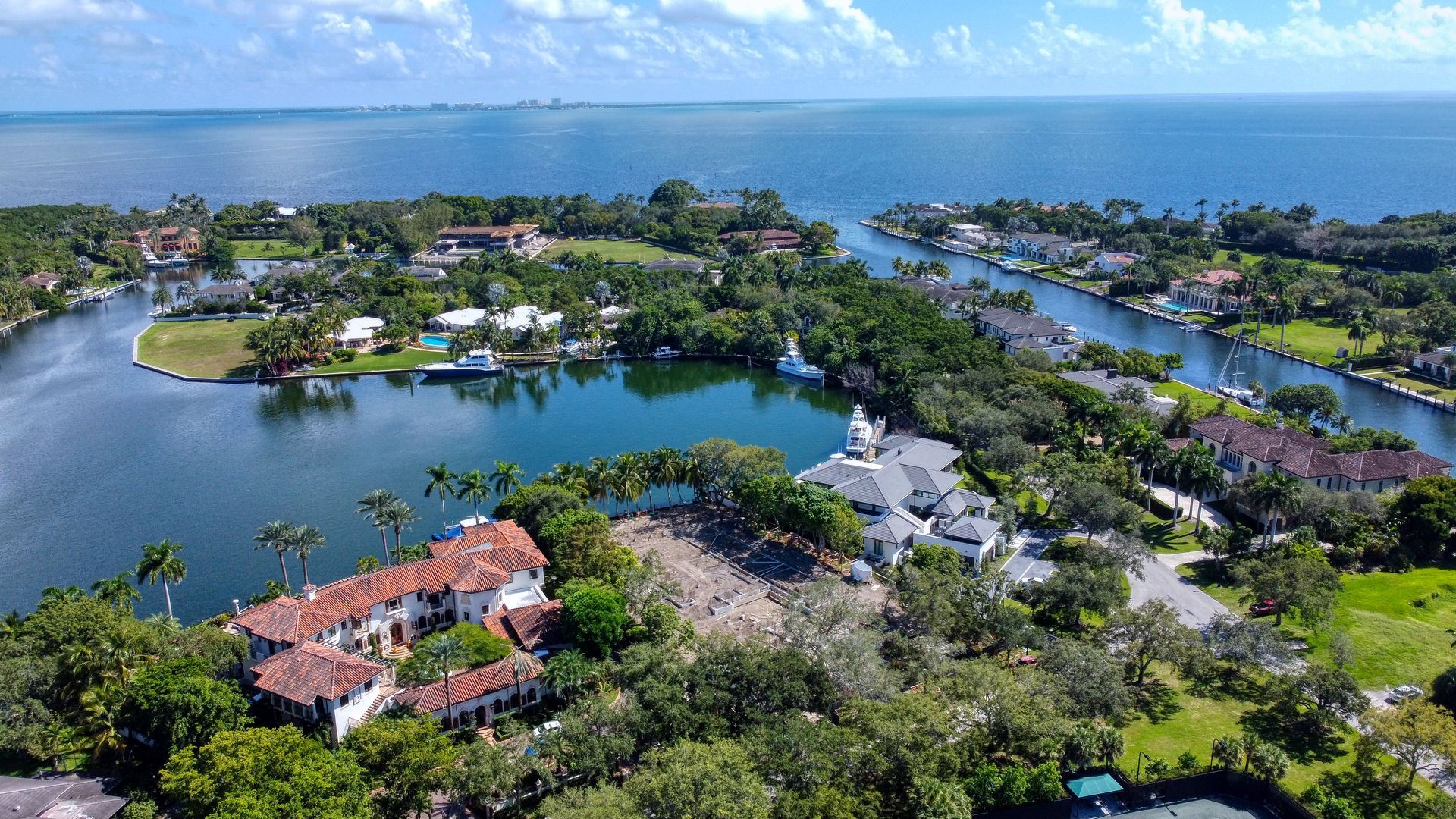 Aerial view of waterfront homes, canals, and waterway leading to ocean. Lush green trees and blue water.