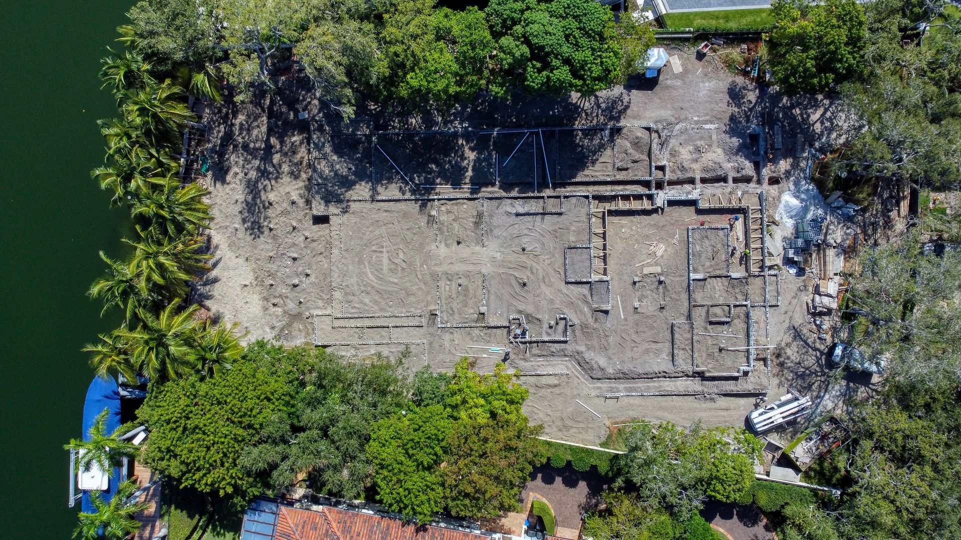 Overhead view of a construction site on a small island, surrounded by trees and water.