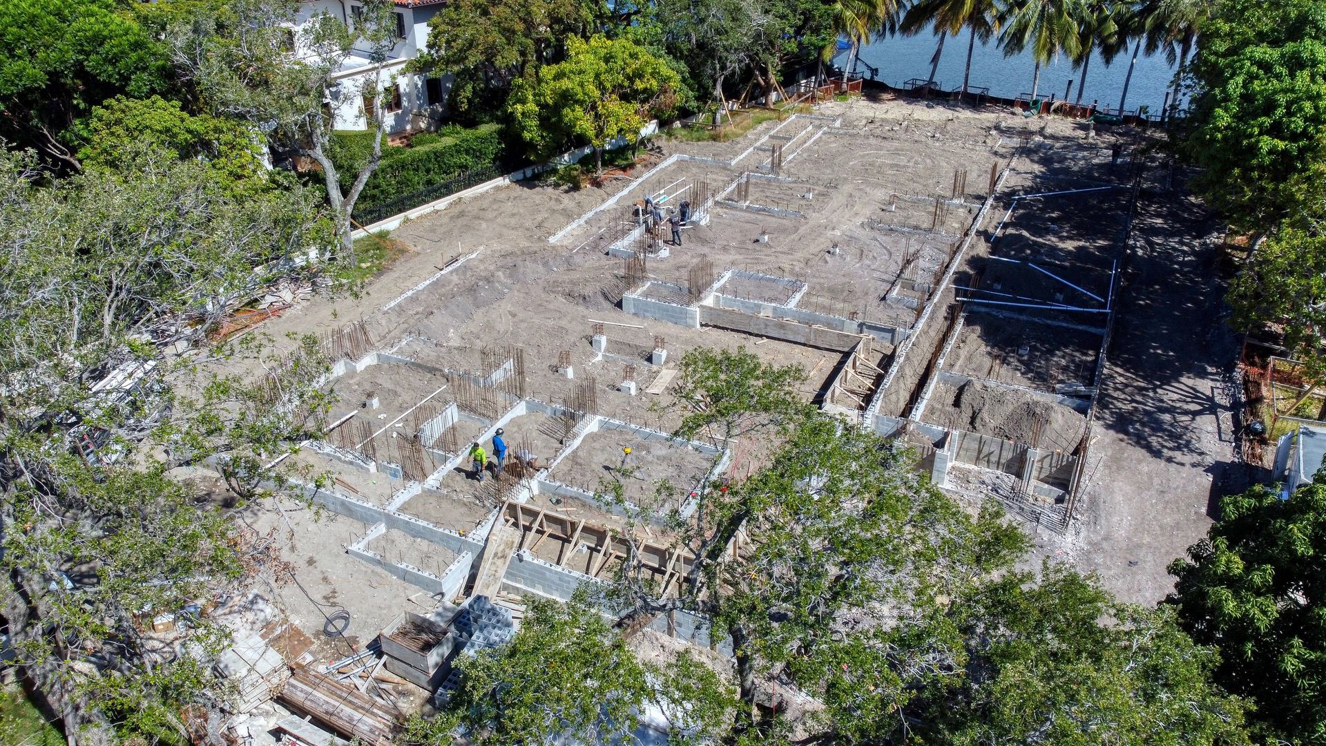 Aerial view of construction site with exposed foundation, surrounded by trees.