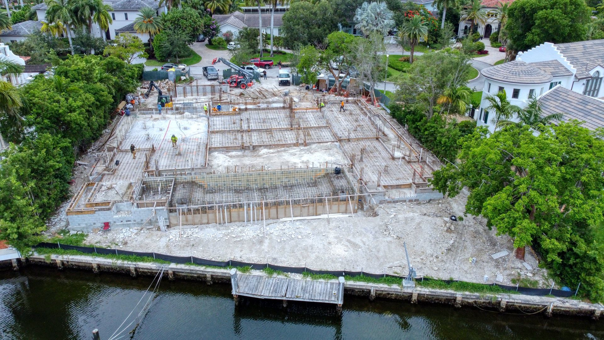 Construction site next to water; concrete foundation with wooden frames; workers visible.
