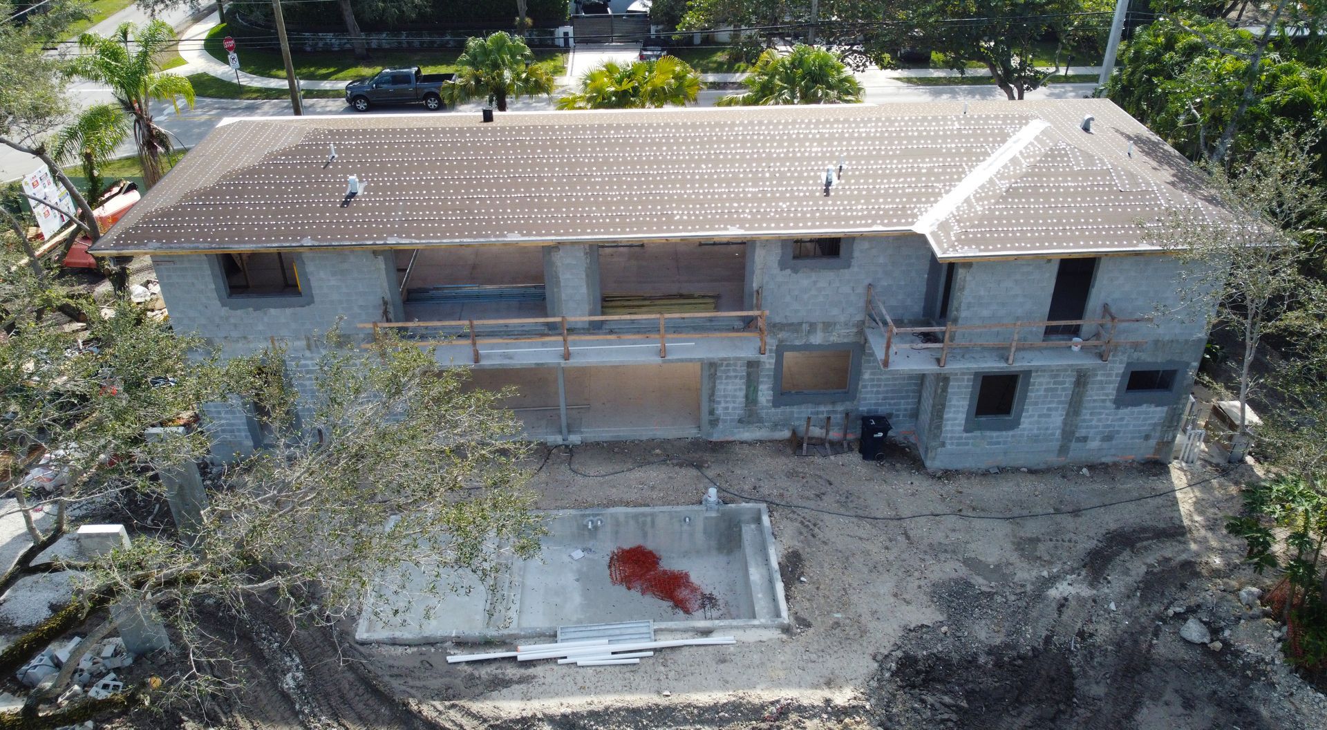Aerial view of a two-story concrete building under construction with a rectangular pool.