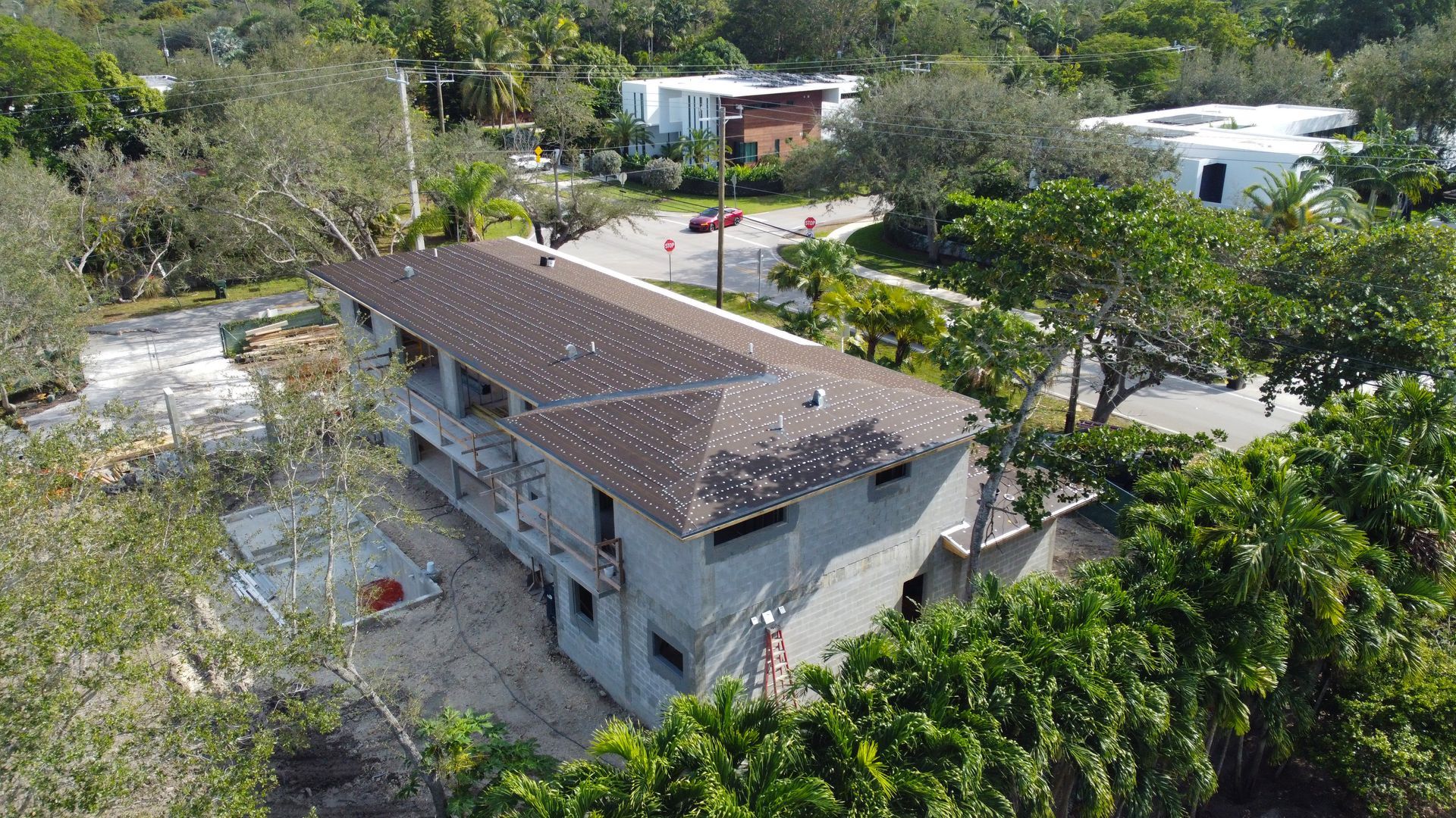 Aerial view of a two-story building under construction, with a dark brown roof and surrounded by greenery.