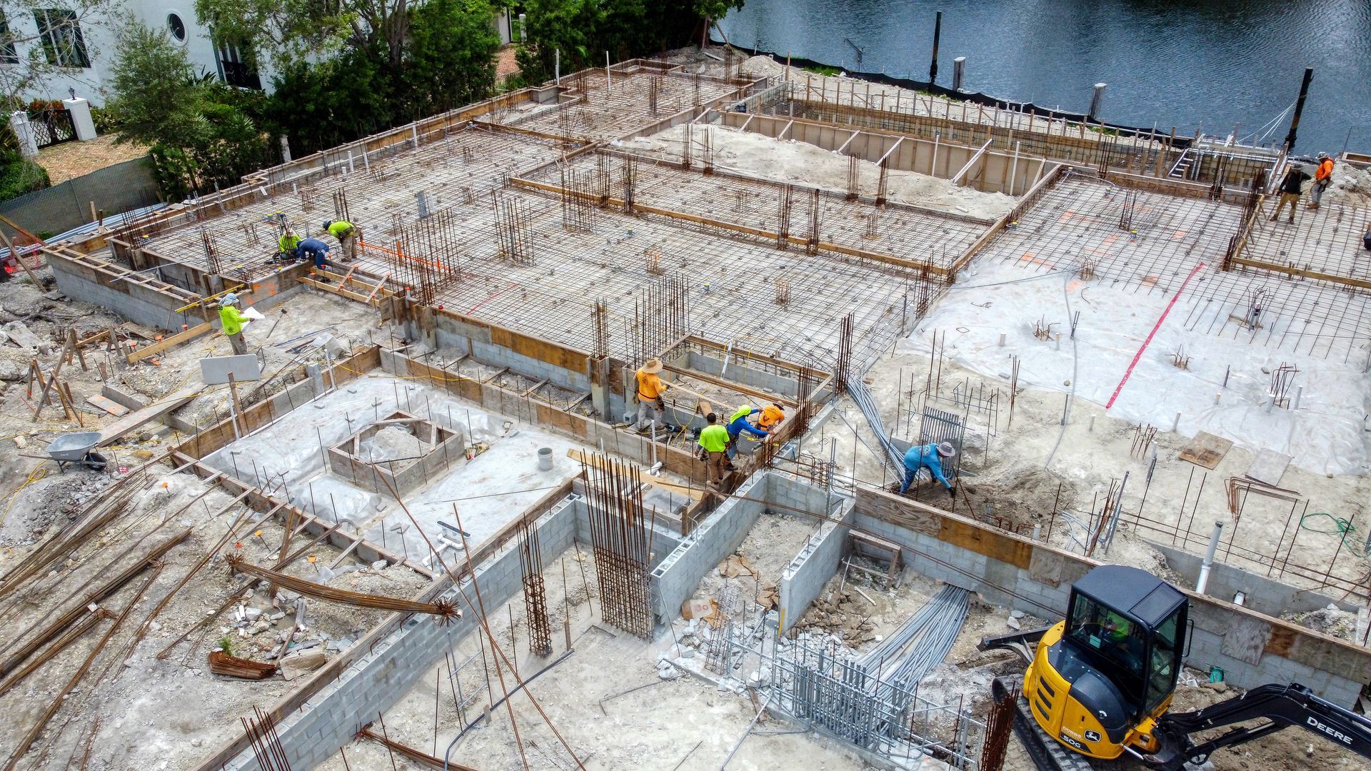 Construction site with workers, machinery, and foundation framework near water.