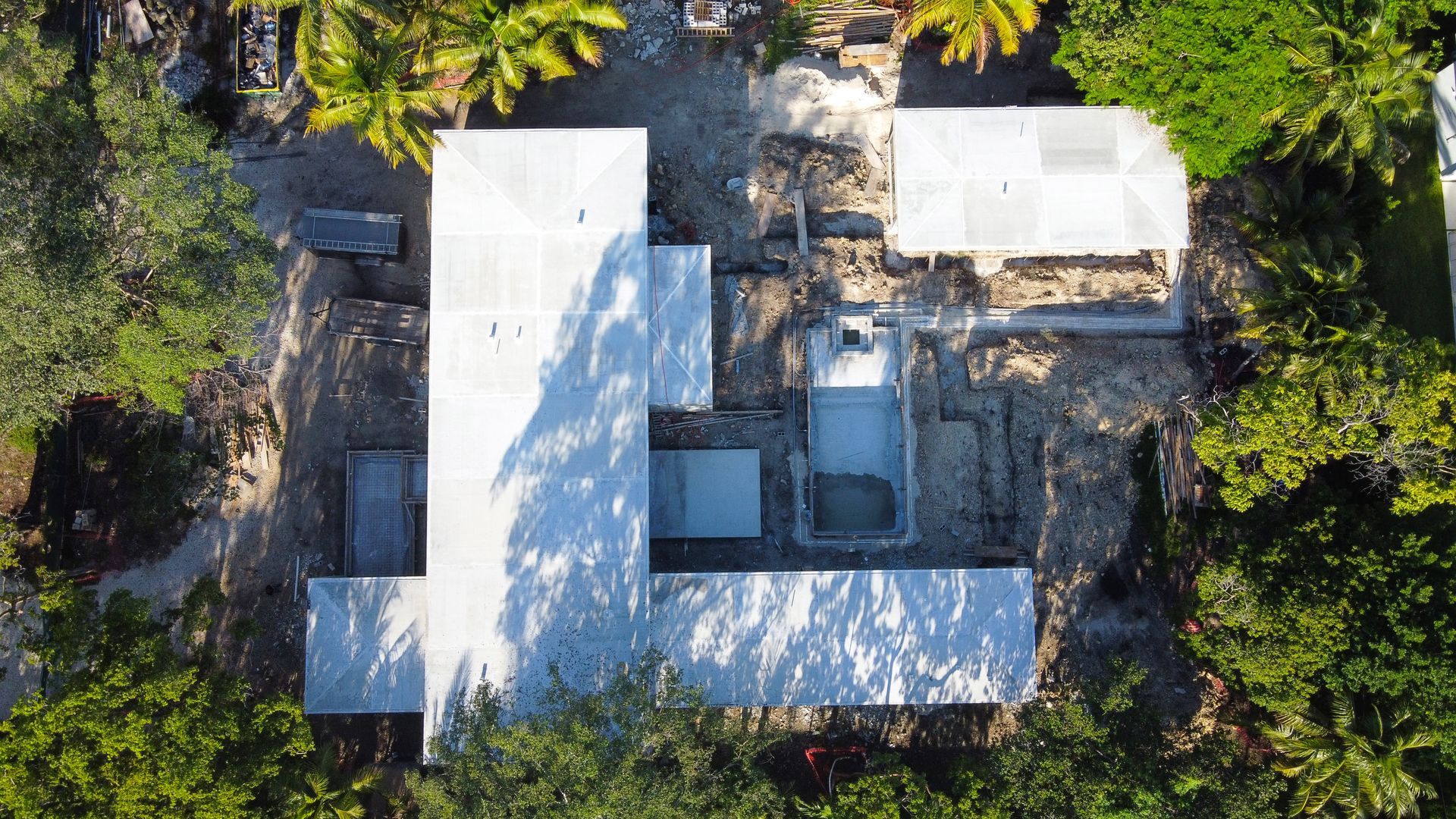 Overhead view of a modern building with multiple sections, light-colored roofs, surrounded by trees.