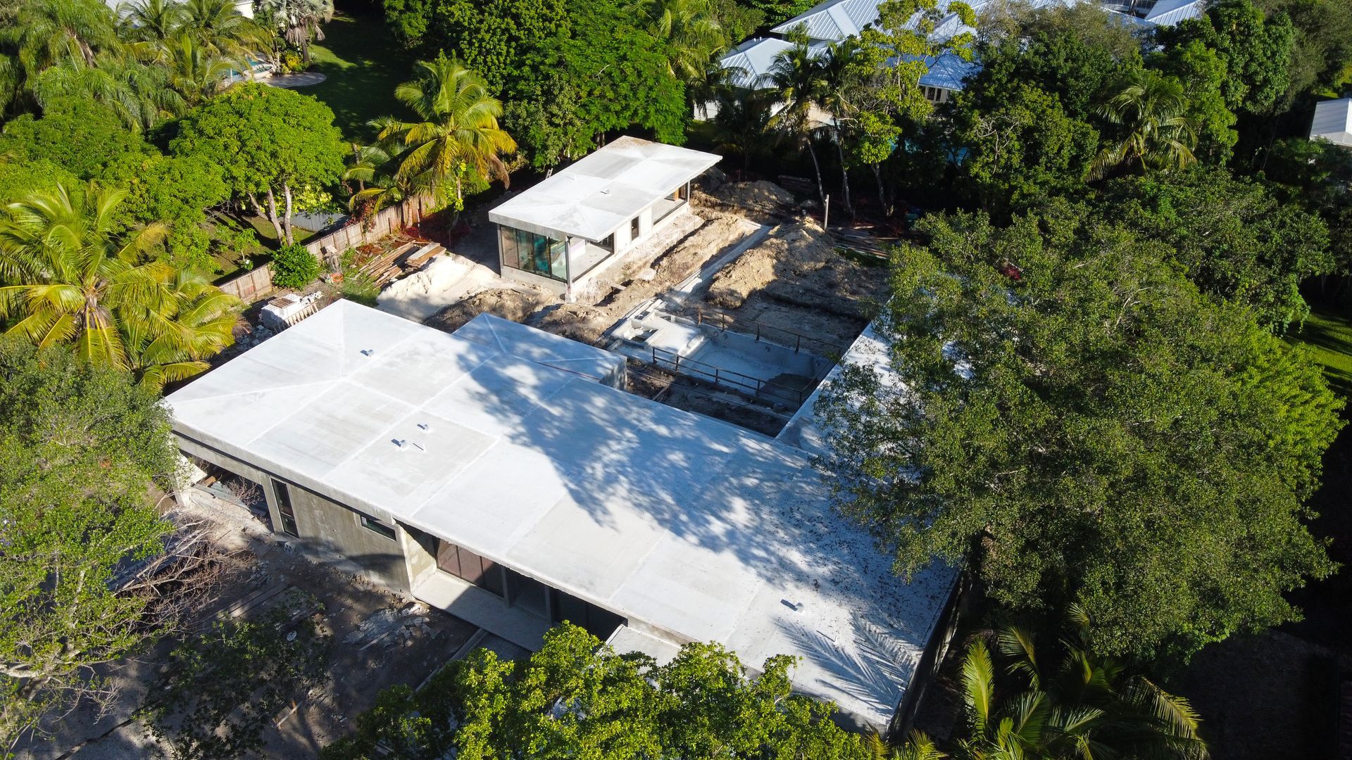 Aerial view of a home under construction with a large, flat roof and surrounding trees.