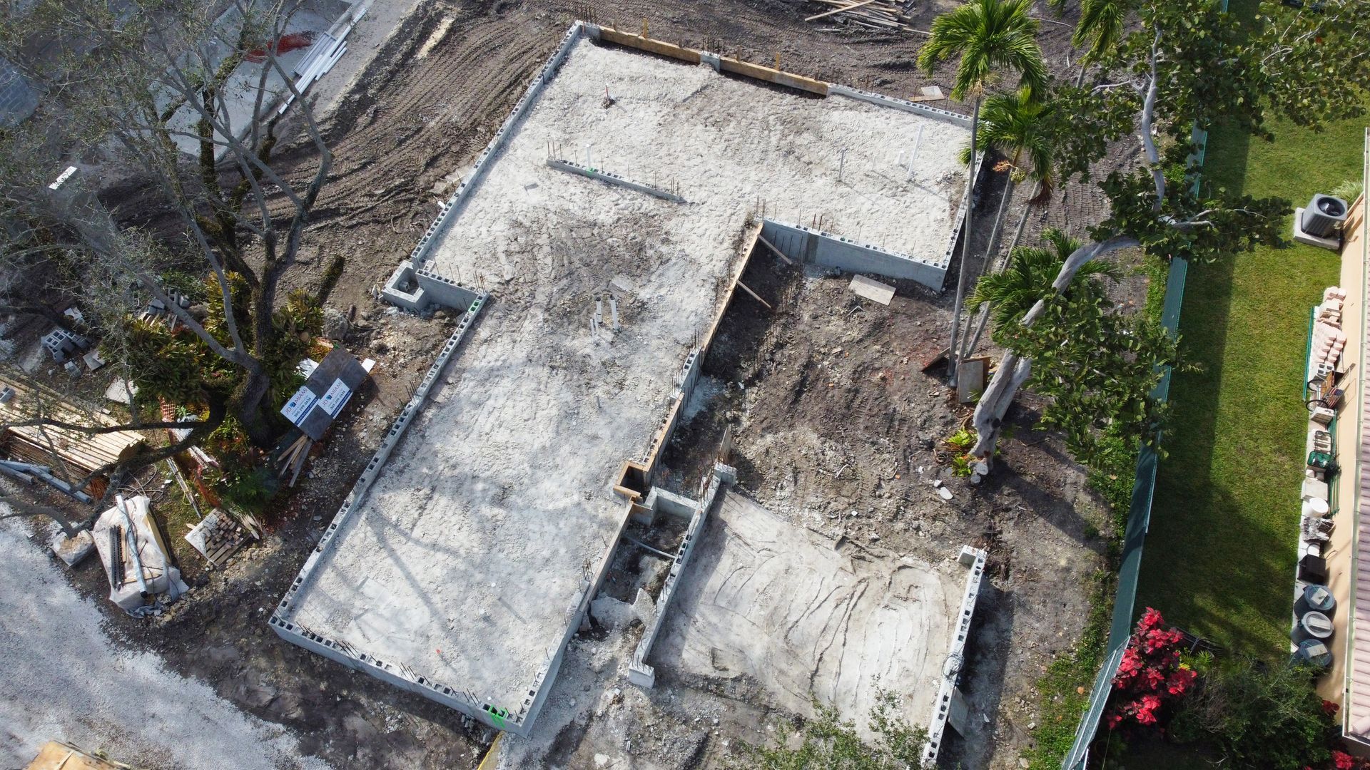 Overhead view of a concrete foundation for a building under construction, surrounded by dirt and construction materials.