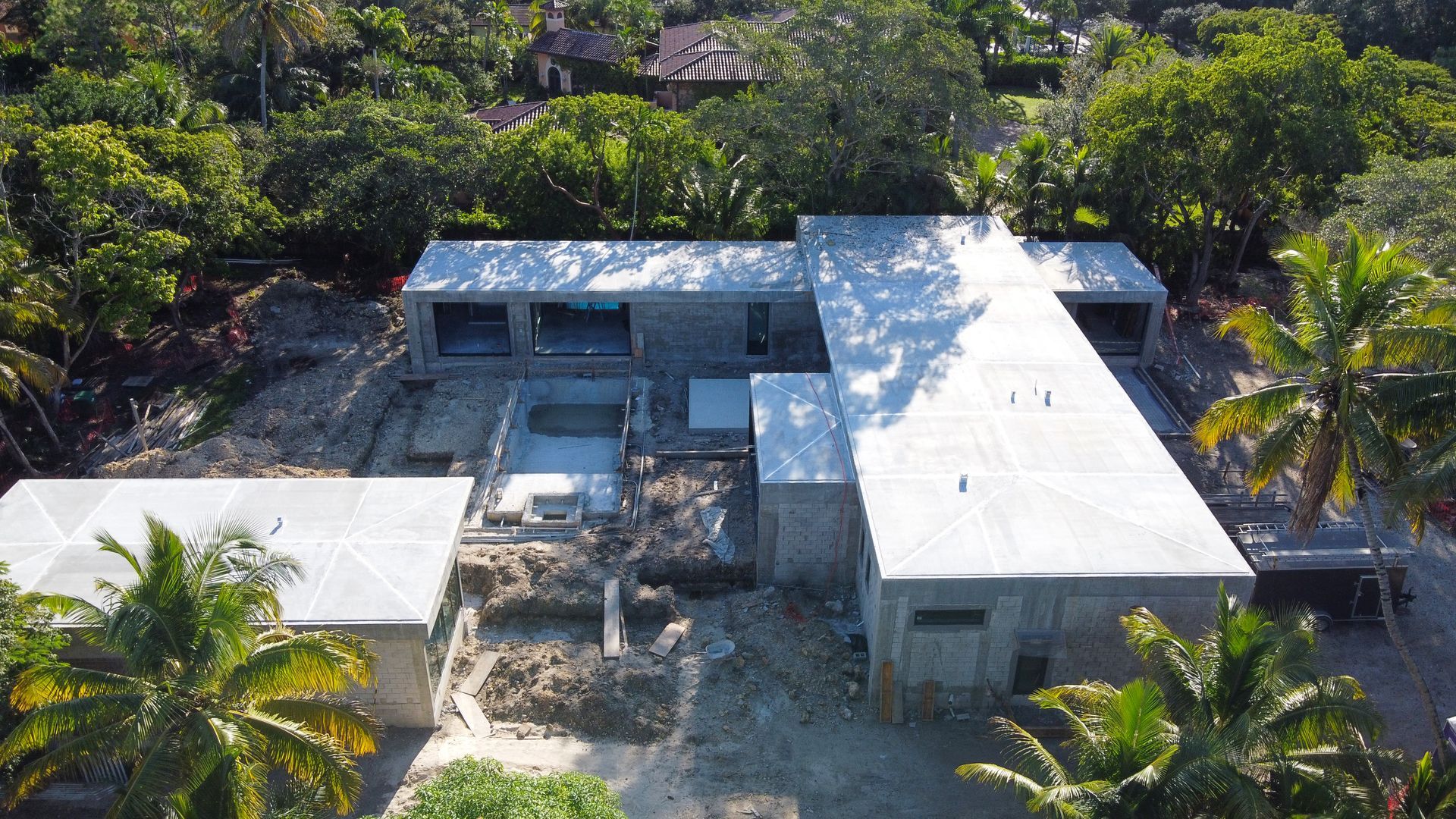 Aerial view of a contemporary house under construction; concrete structure with a white roof in a tropical setting.
