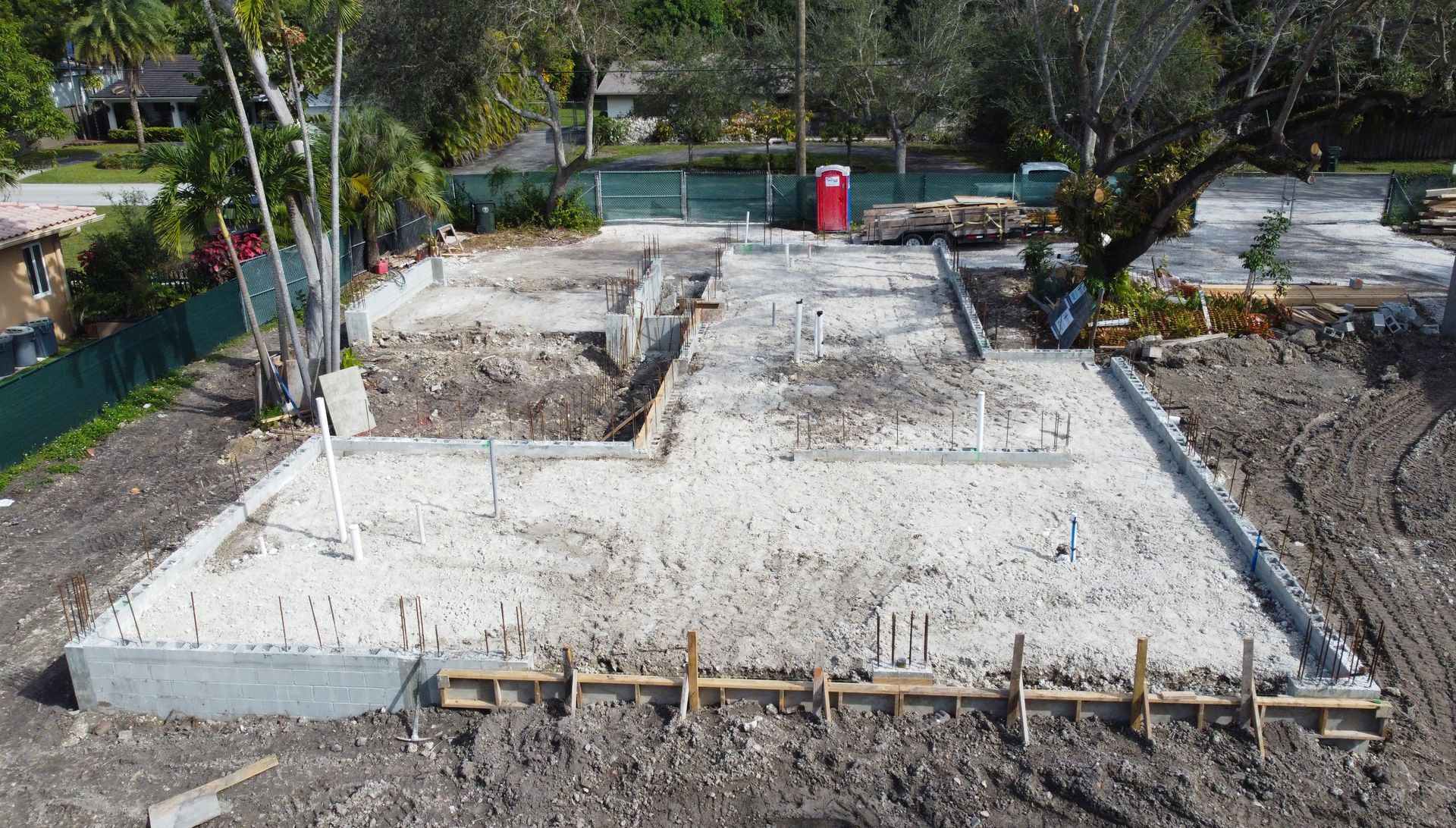 Construction site with concrete foundation and plumbing, dirt and a few trees.