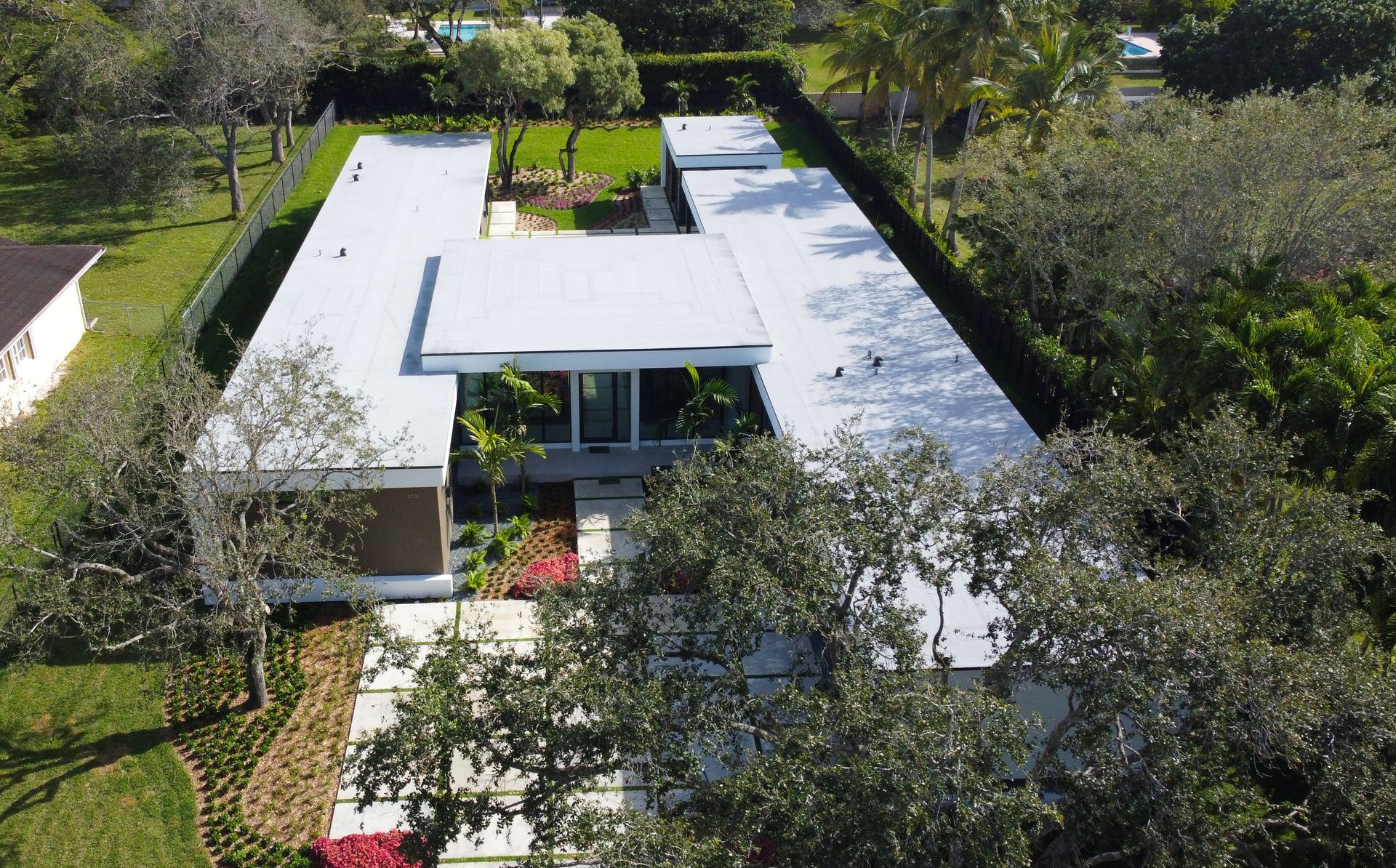 Modern home with flat white roof, surrounded by green trees and foliage.