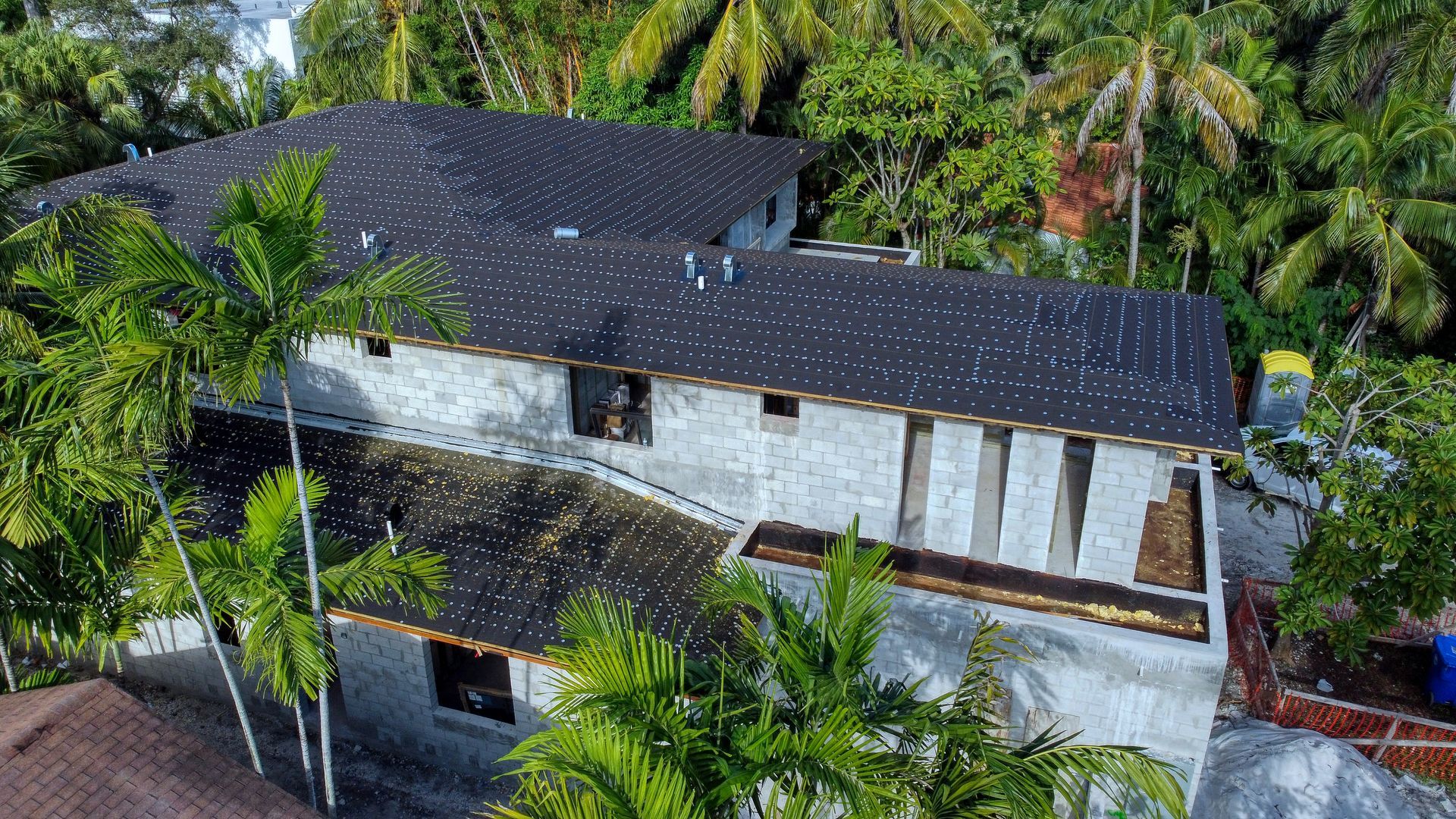 Multi-story building with dark speckled roof, surrounded by lush green trees.