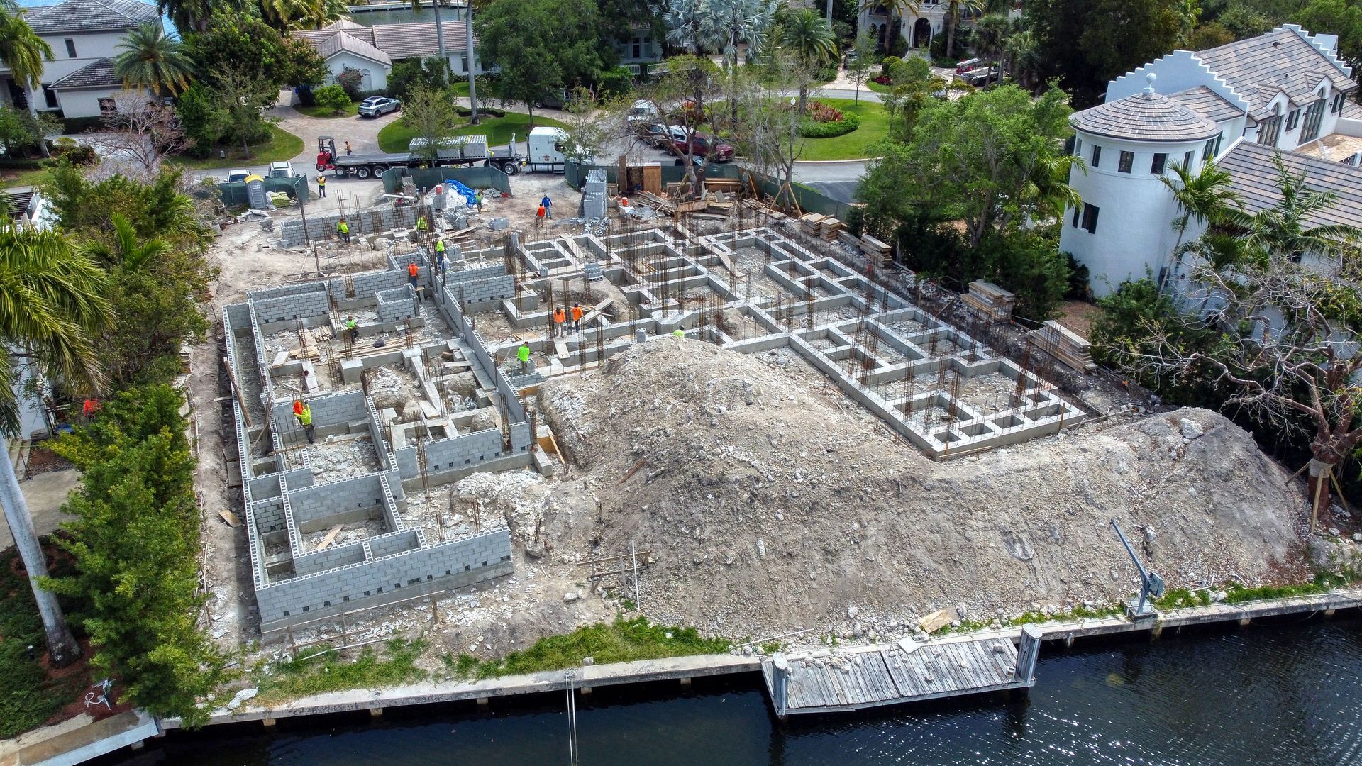 Construction site with building foundations, rubble, and workers near a waterway.