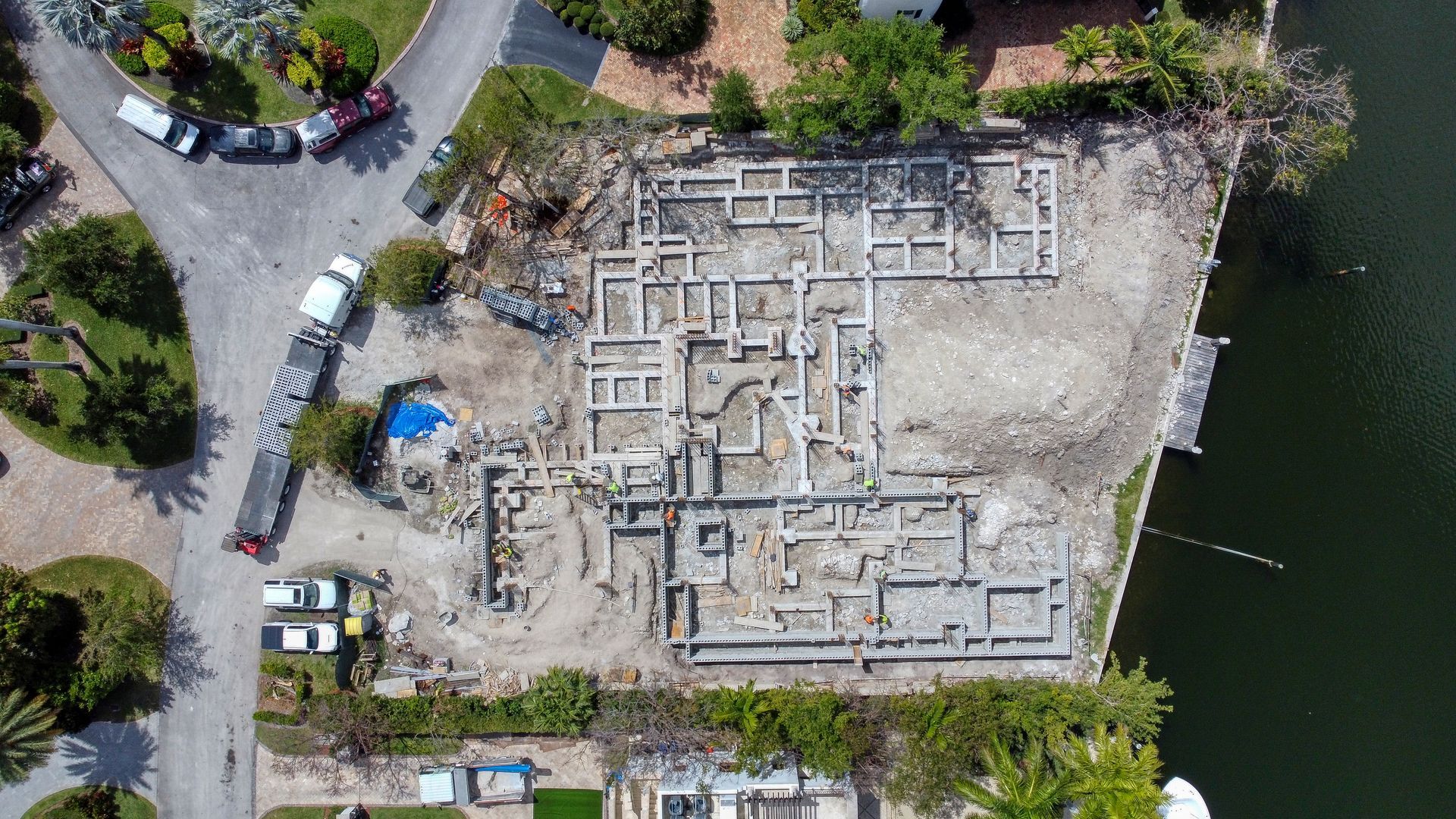 Aerial view of a building foundation. Concrete structures on dirt ground, next to water.