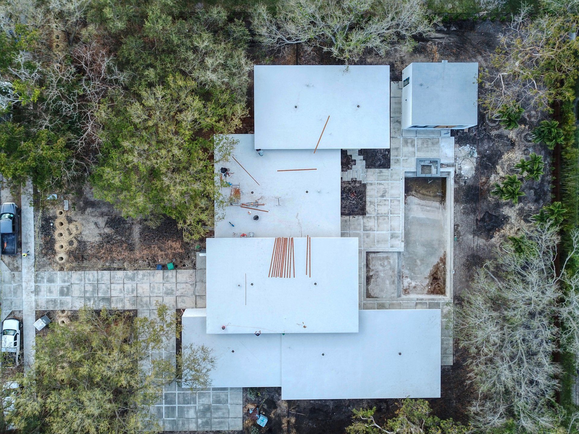 Aerial view of a rectangular building with a concrete patio surrounded by trees and a long driveway.