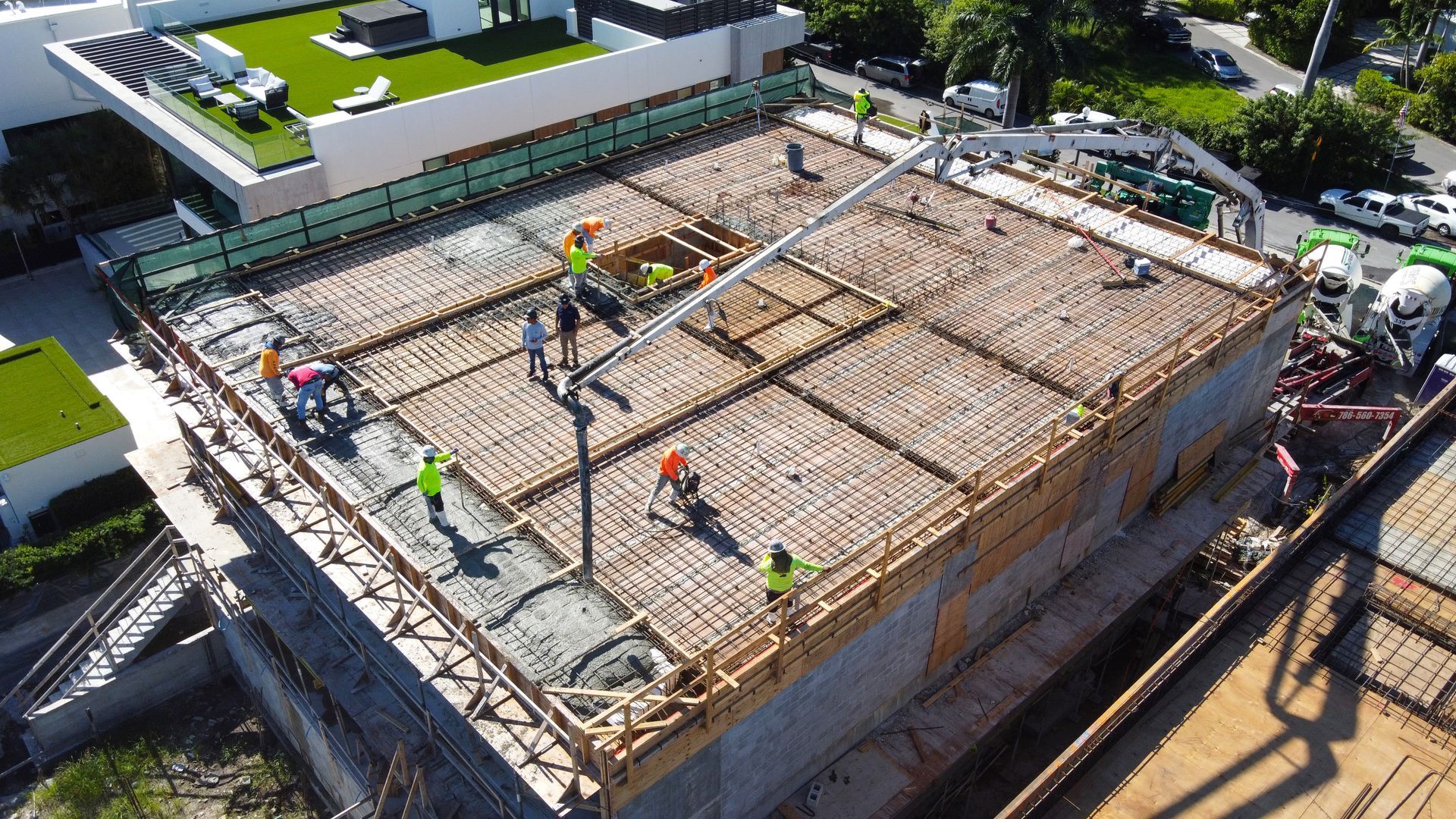 Construction site with workers pouring concrete on a building's roof; concrete pump in use.
