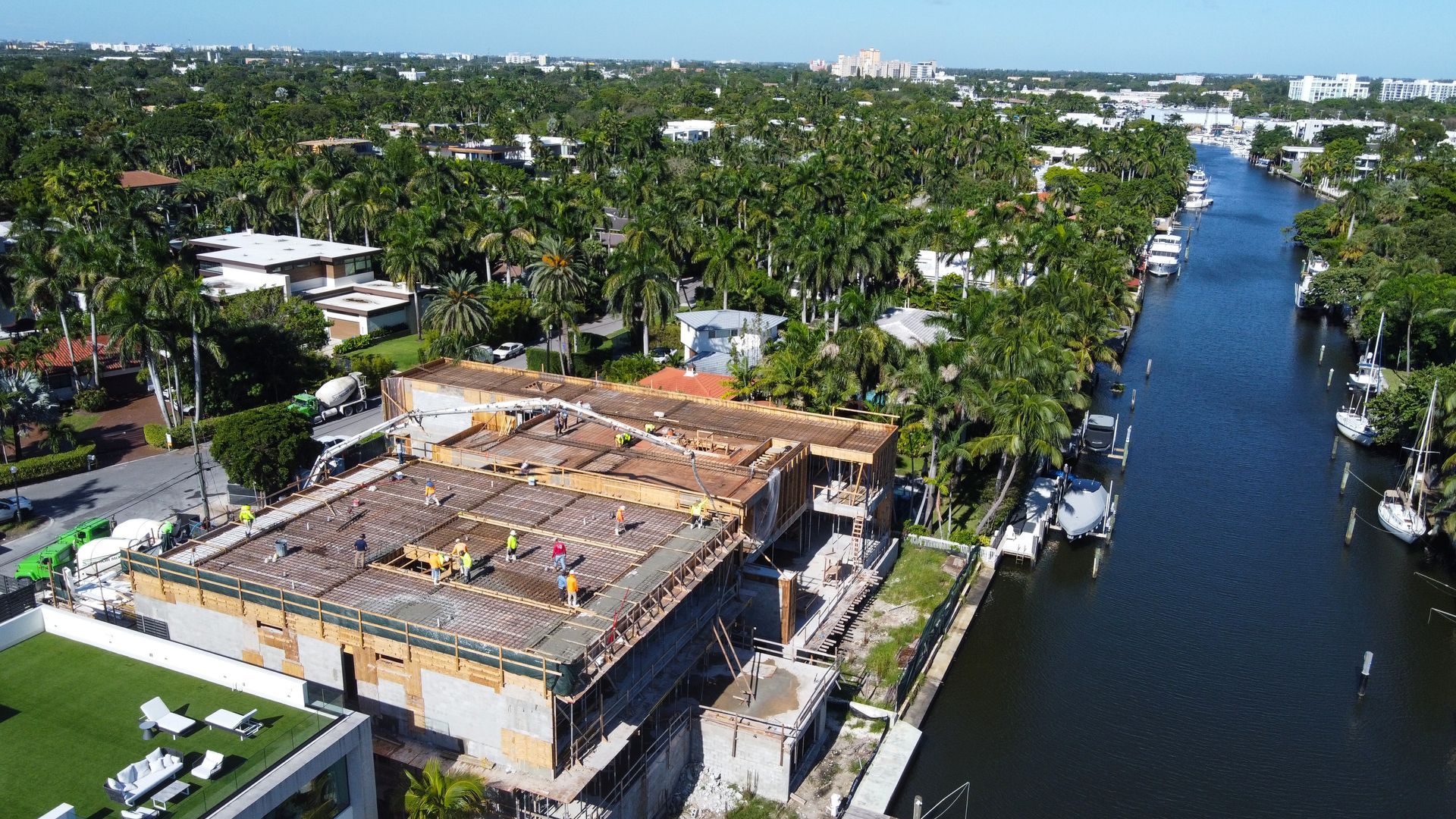 Aerial view of a house under construction next to a waterway lined with palm trees and boats.