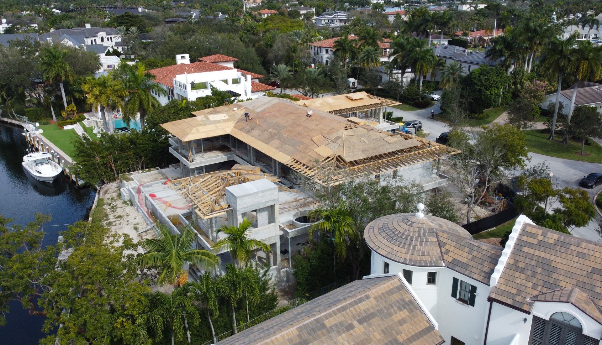 Aerial view of a home under construction with exposed roof structure, near a waterway and other houses.