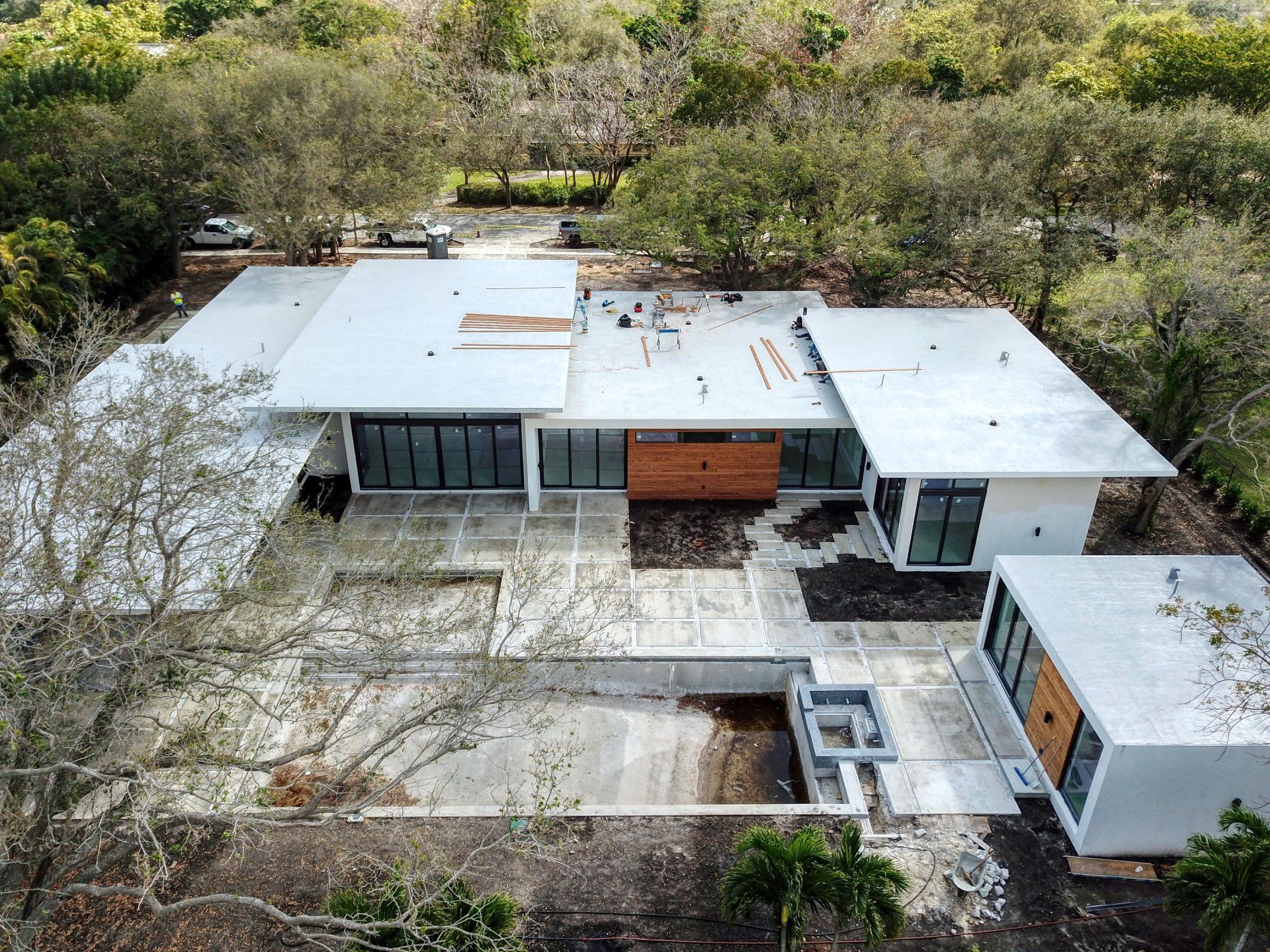 Aerial view of a modern house with a flat roof, surrounded by trees and a concrete patio.