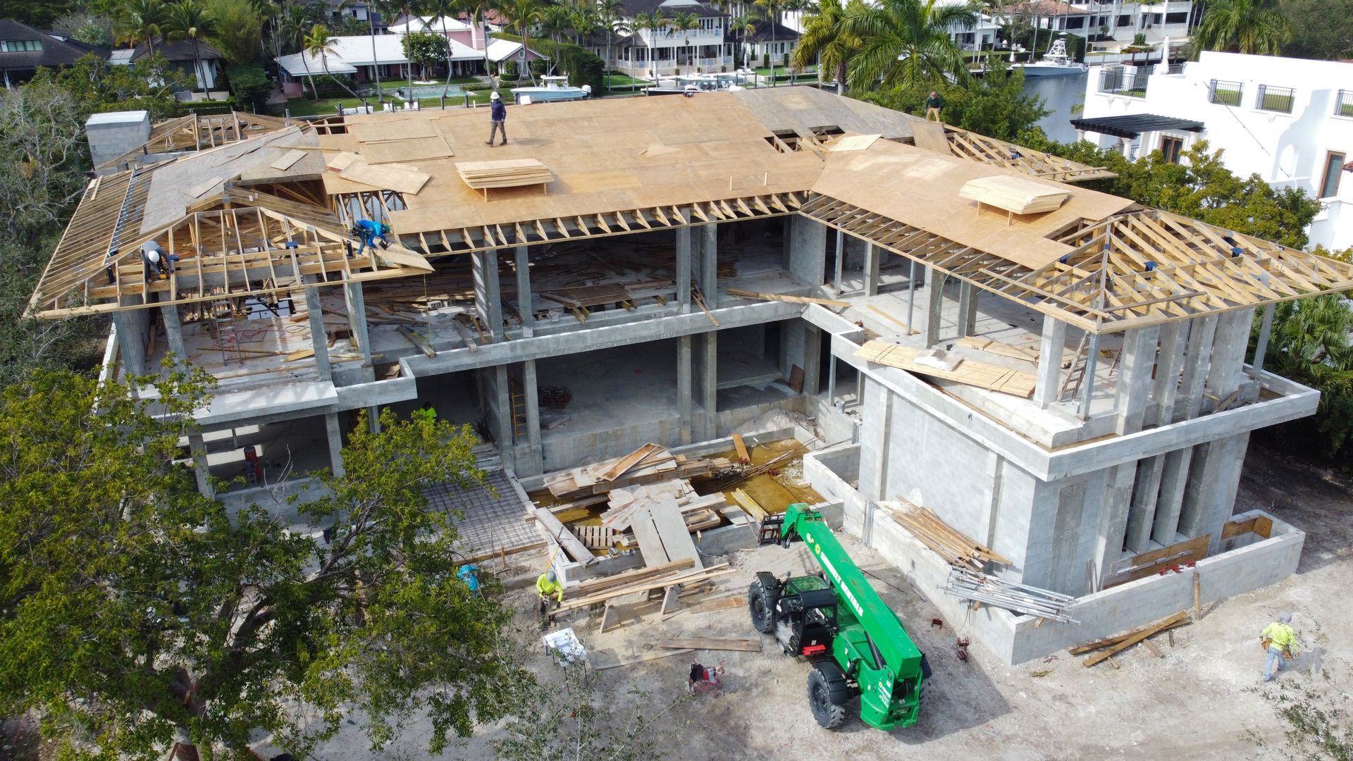 Construction site with a two-story concrete building under construction; workers on roof, green forklift.