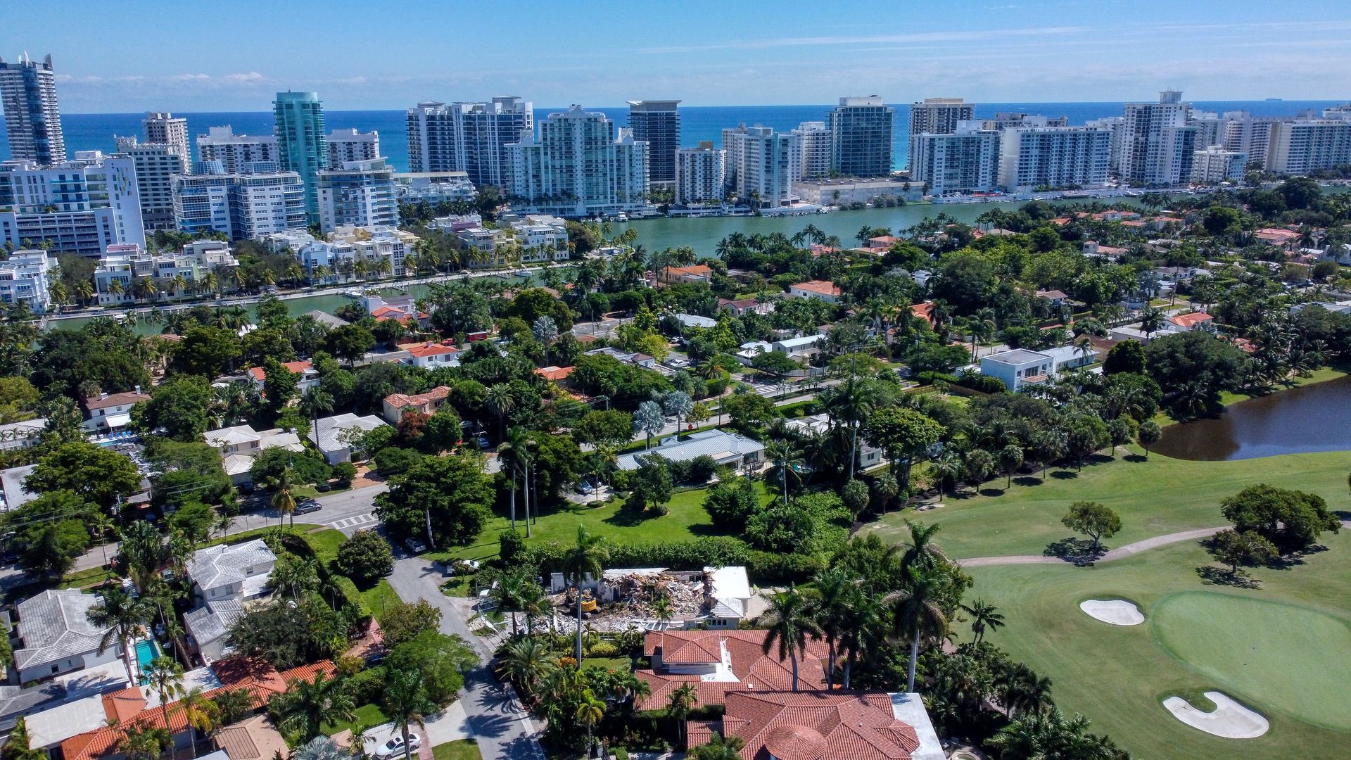 An aerial view of a residential area with a golf course and a city in the background.