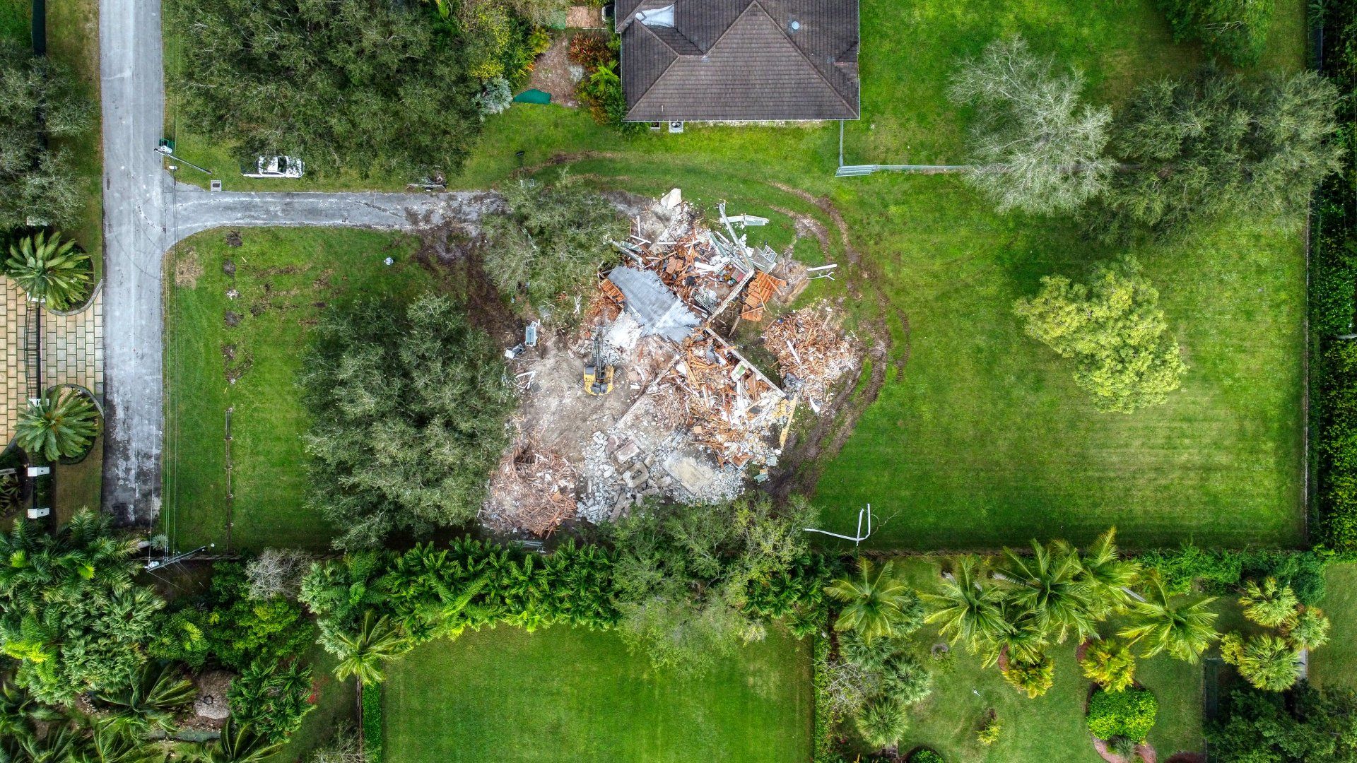 Overhead view of a house destroyed on a grassy lot, debris scattered.
