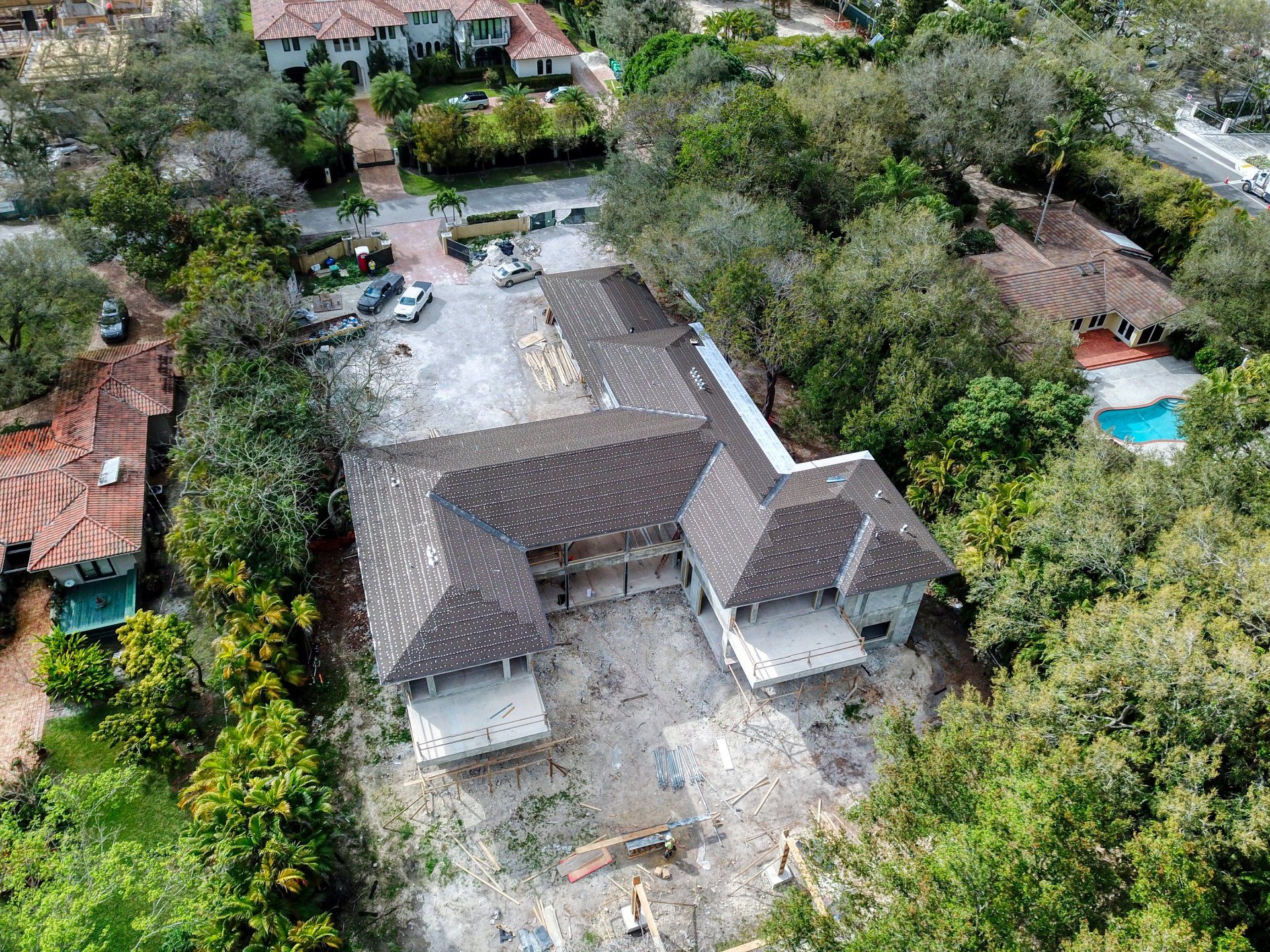 Aerial view of a home under construction surrounded by trees and neighboring houses.