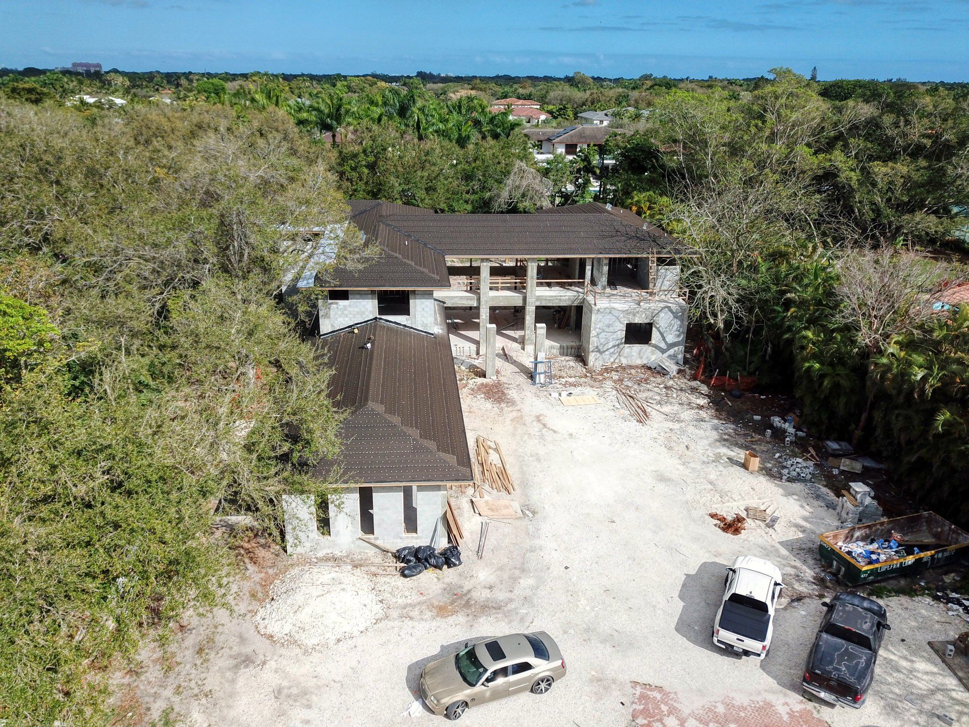 Aerial view of a partially constructed two-story building surrounded by trees and construction vehicles on a dirt lot.