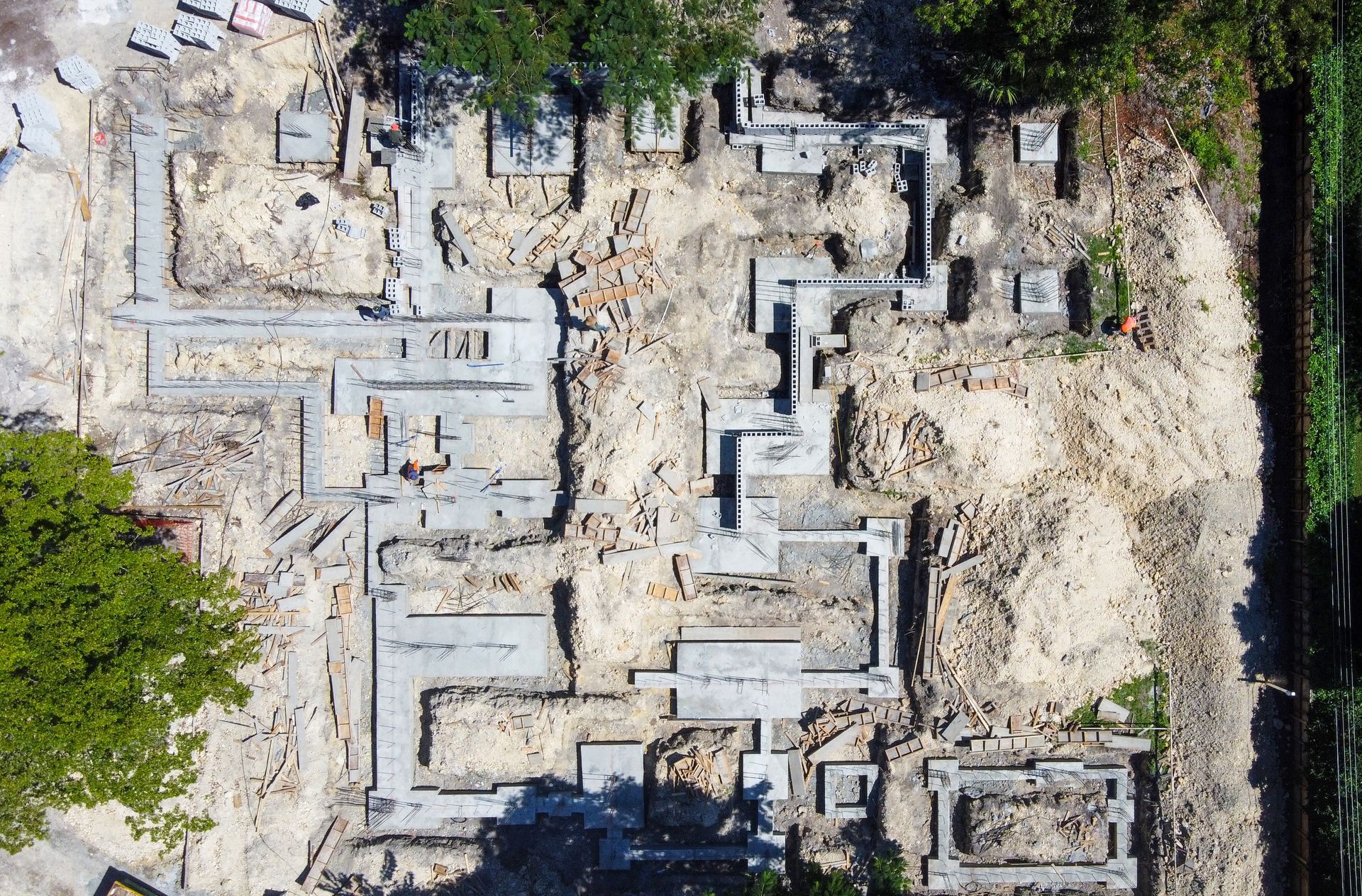 Overhead view of a construction site foundation. Concrete forms are surrounded by debris and some greenery.