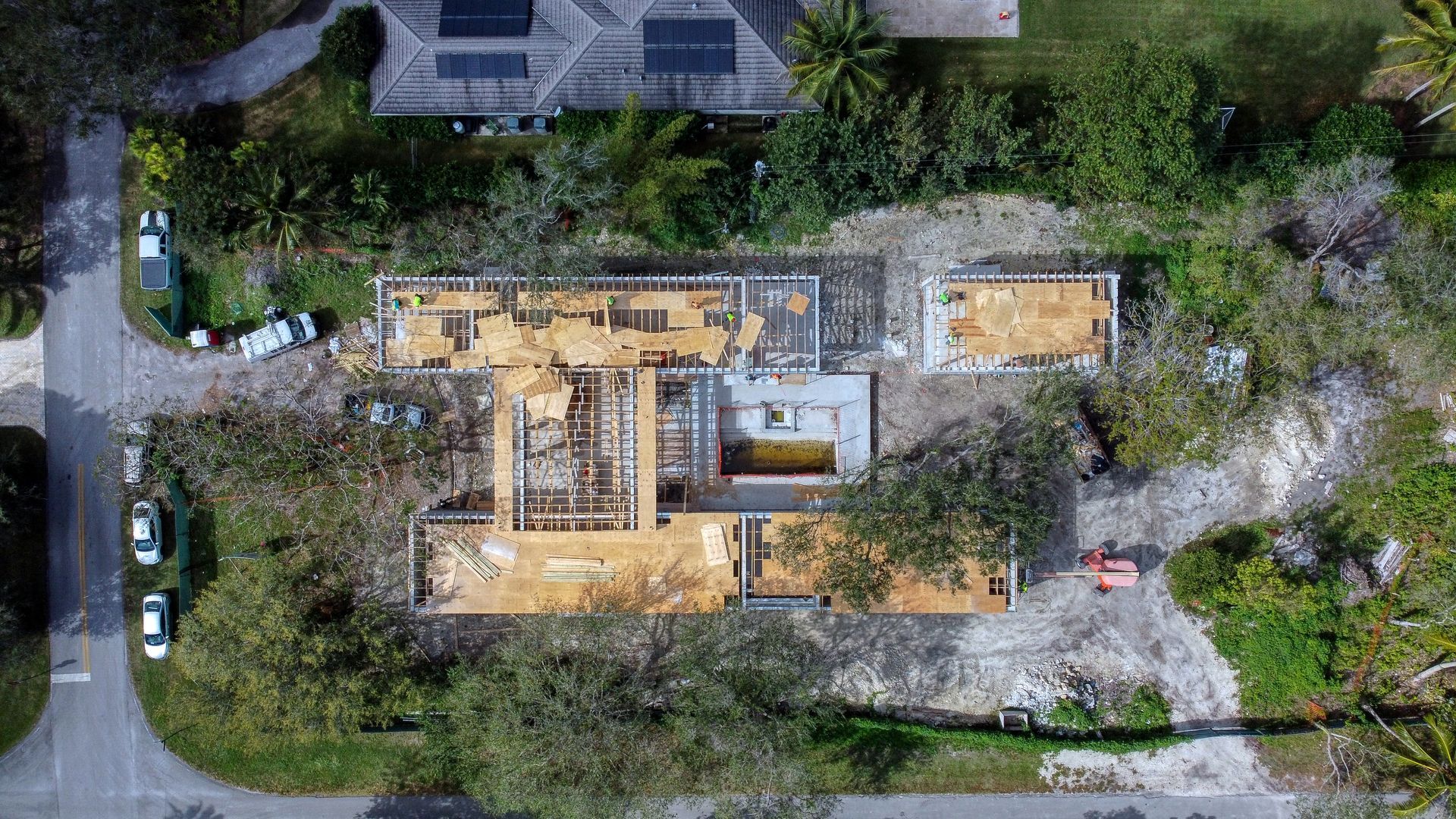 Aerial view of a home under construction; wooden beams exposed, surrounded by debris and greenery.