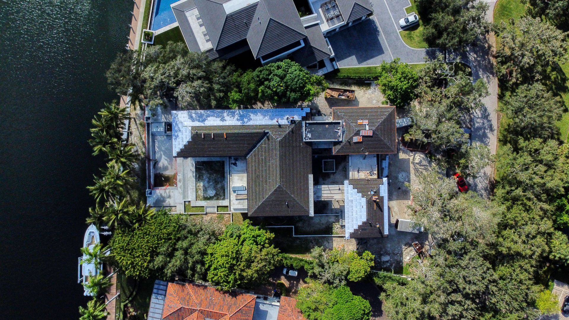 Aerial view of a house with a dark roof surrounded by trees and a waterway.