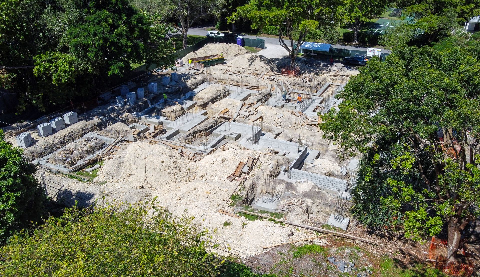 Overhead view of a construction site with scattered concrete blocks and earth surrounded by green trees.