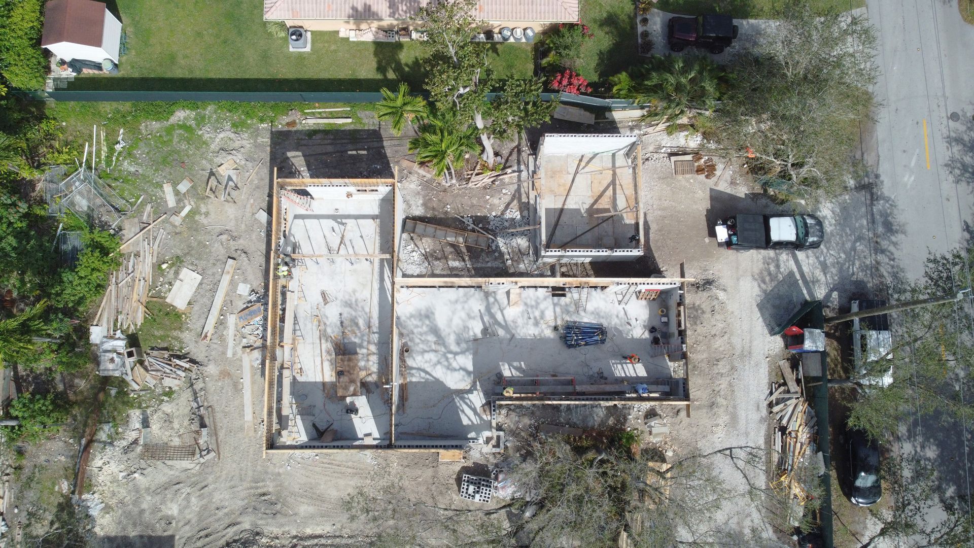 Aerial view of a building's foundation under construction, surrounded by debris and construction vehicles on a sunny day.