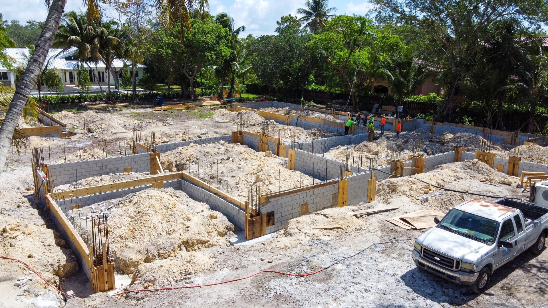 Construction site with concrete foundation and workers; white truck parked nearby.