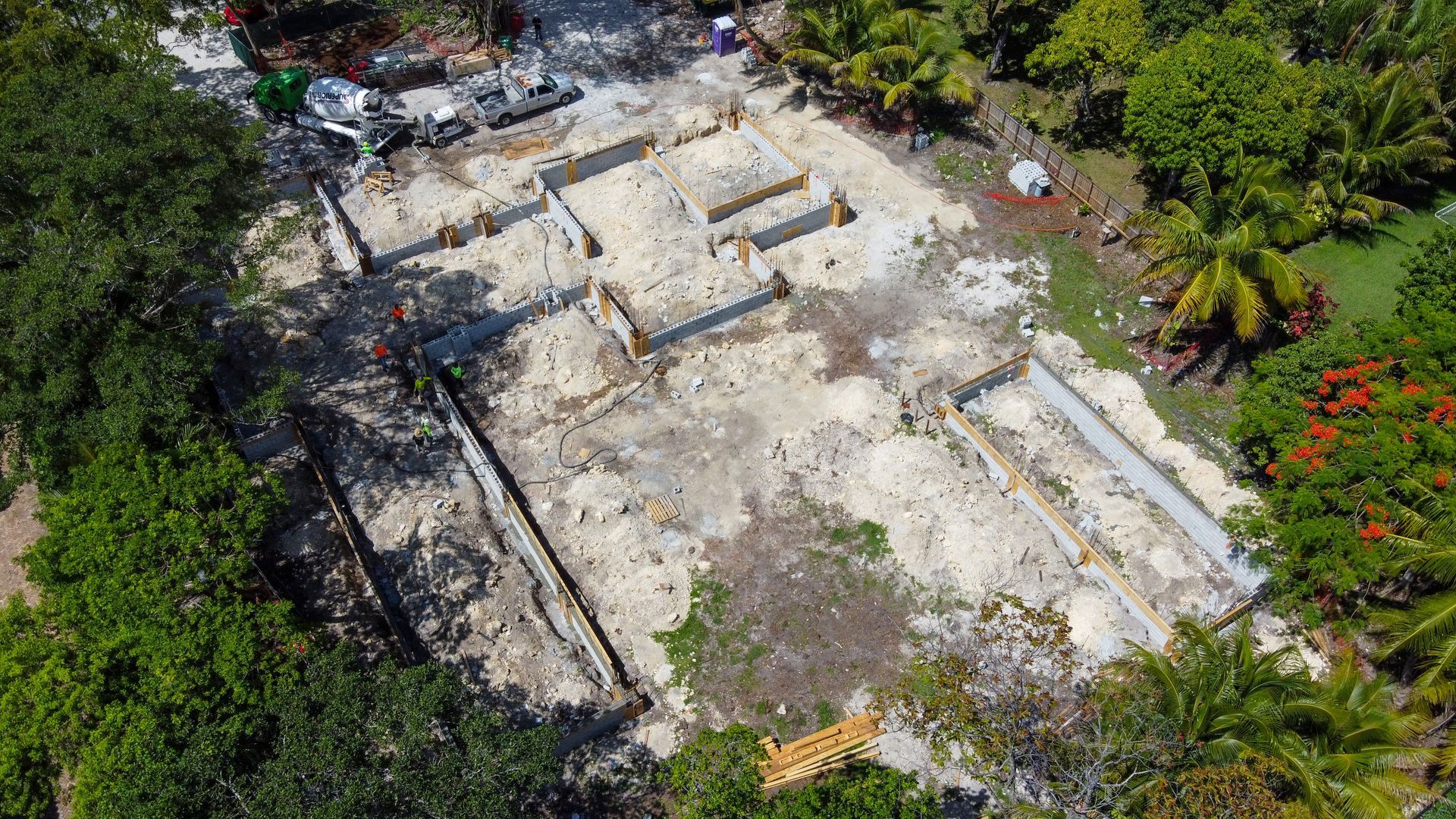 Aerial view of construction site with concrete foundation, surrounded by trees.