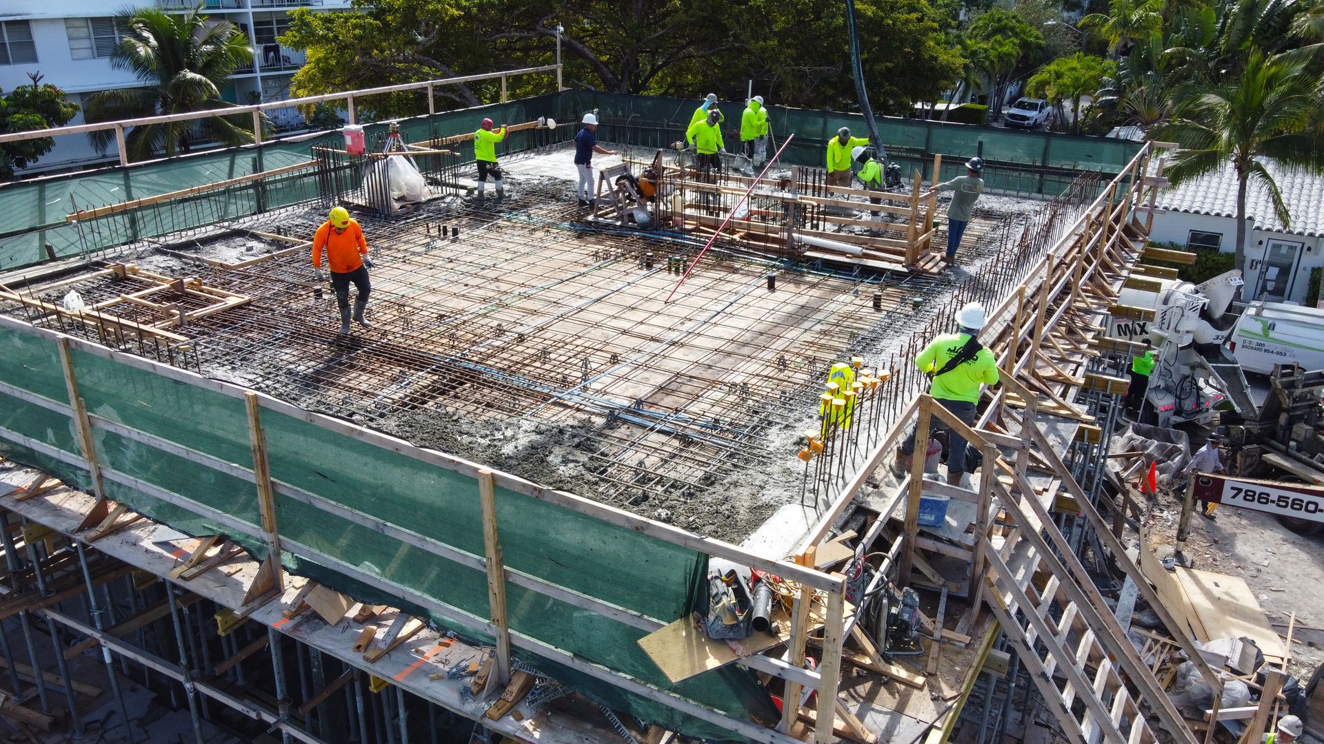 Construction site with workers on a concrete structure. Green safety netting surrounds the structure.