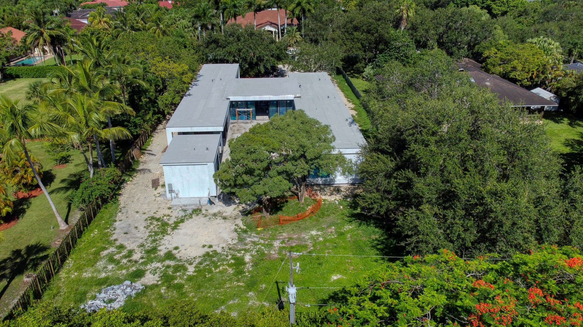 Aerial view of a U-shaped, light-colored house surrounded by trees and a green lawn.