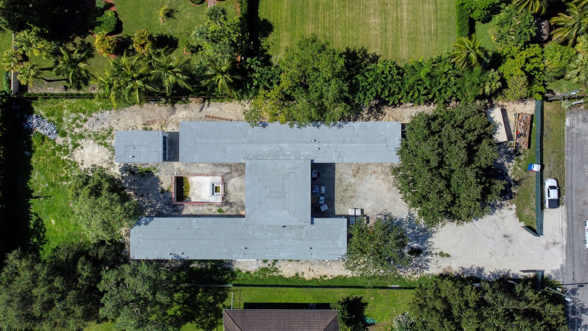 Overhead view of a gray-roofed building surrounded by trees, grass, and a gravel driveway.