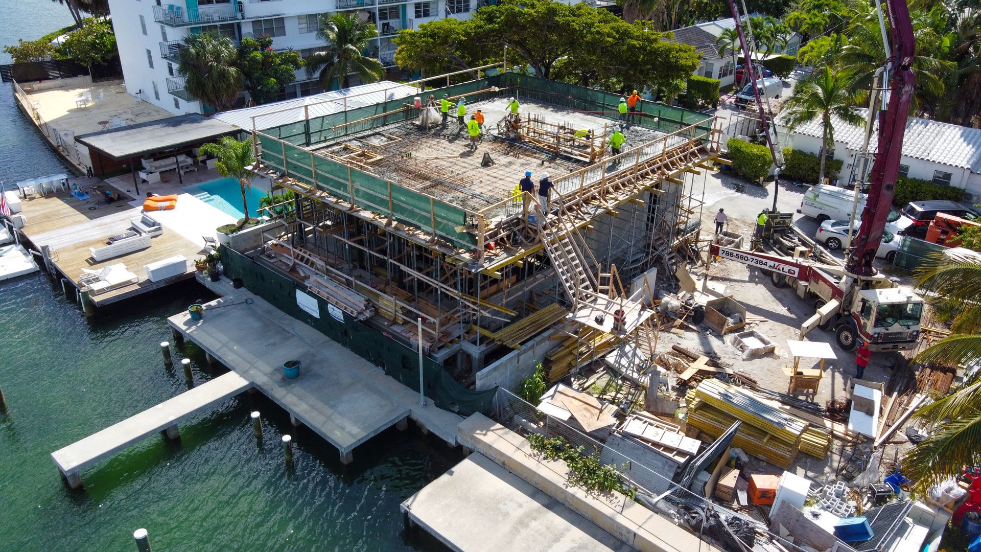 Construction of a multi-story building on a waterfront with workers, scaffolding, and equipment.